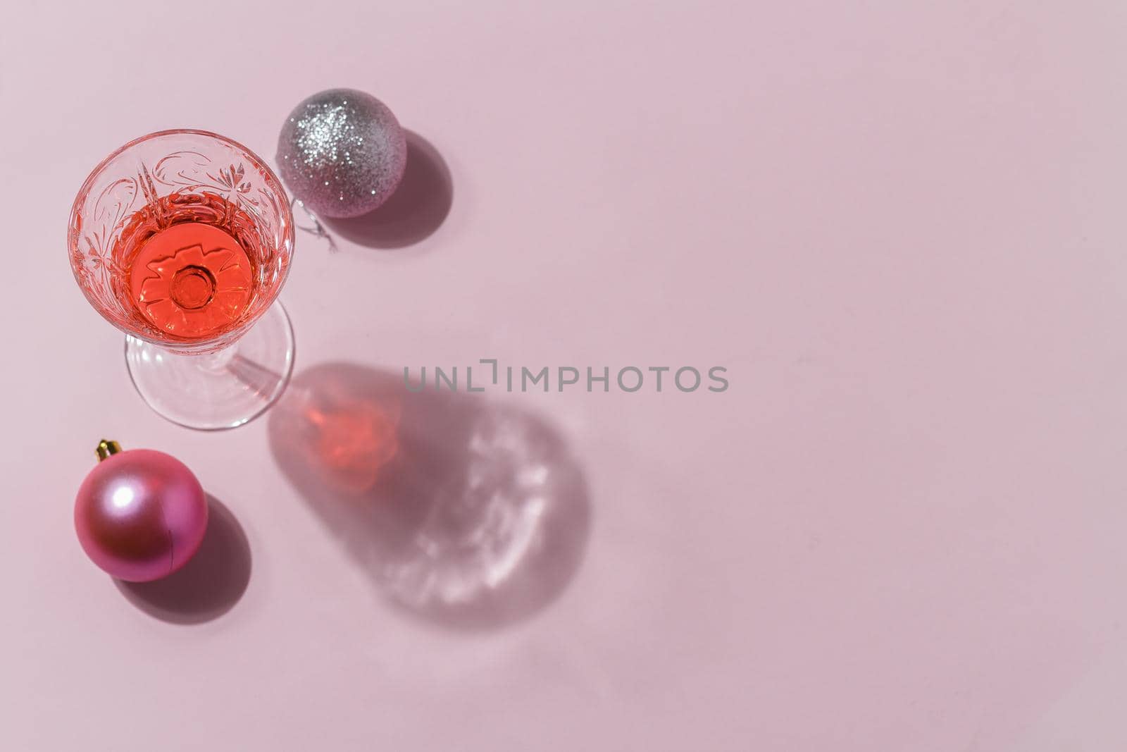 Minimalistic composition of Christmas toys on a pink background with a cocktail in a glass. The concept of celebrating christmas and new year. copy space