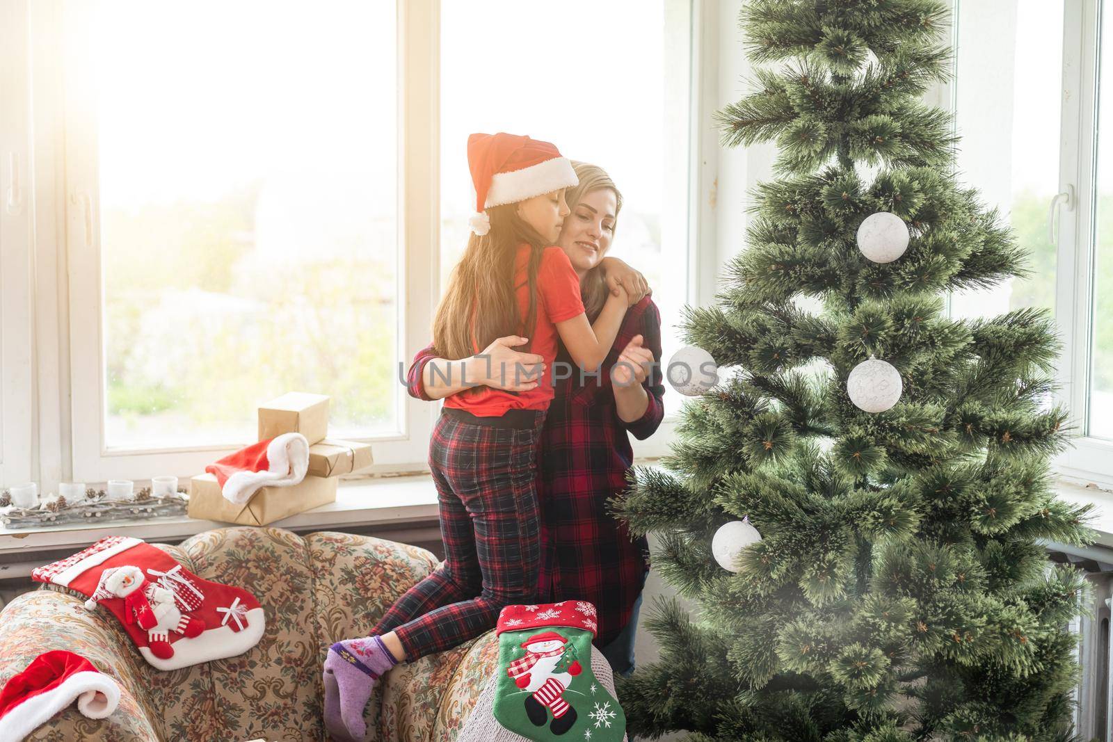 Mother and children decorating the house hang Christmas tree toys on the Christmas tree in a large wooden house.