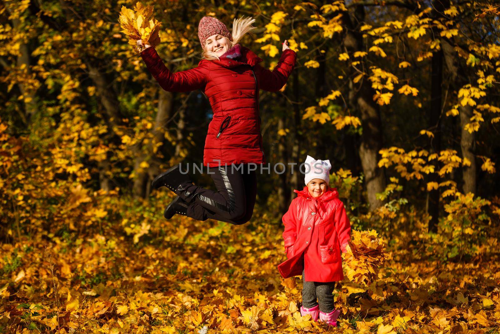 Mother and daughter having fun in the autumn park among the falling leaves