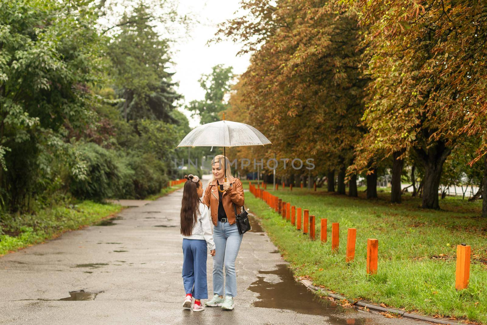 Cheerful mother and her little daughter having fun together in the autumn background under the umbrella. Happy family in the fall background by Andelov13