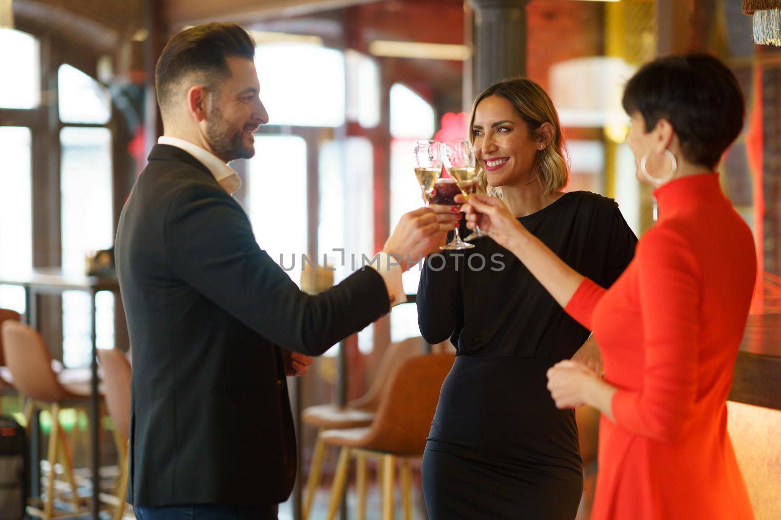 Group of happy elegant friends clinking glasses with champagne and celebrating reunion while gathering in luxury bar and looking at each other