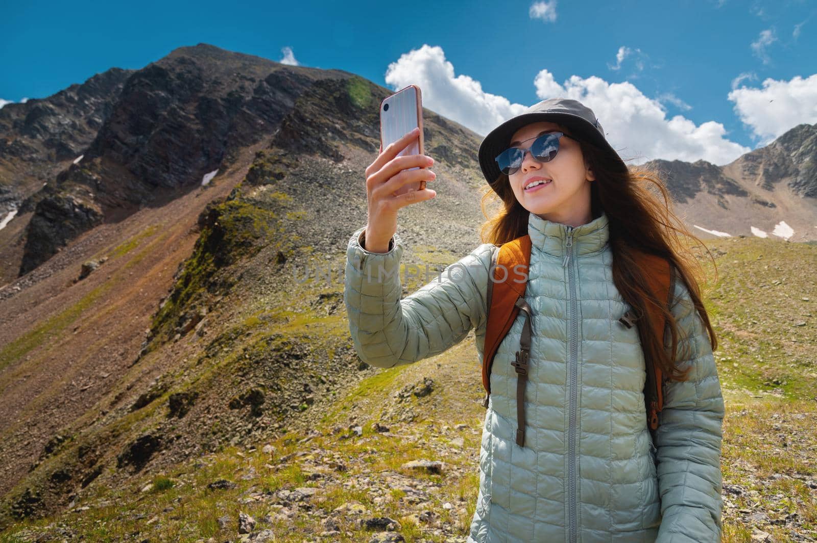 Beautiful happy hiker woman taking a selfie hiking a mountain at vacation. Girl wearing hat and backpack taking a self portrait smiling at the camera by yanik88