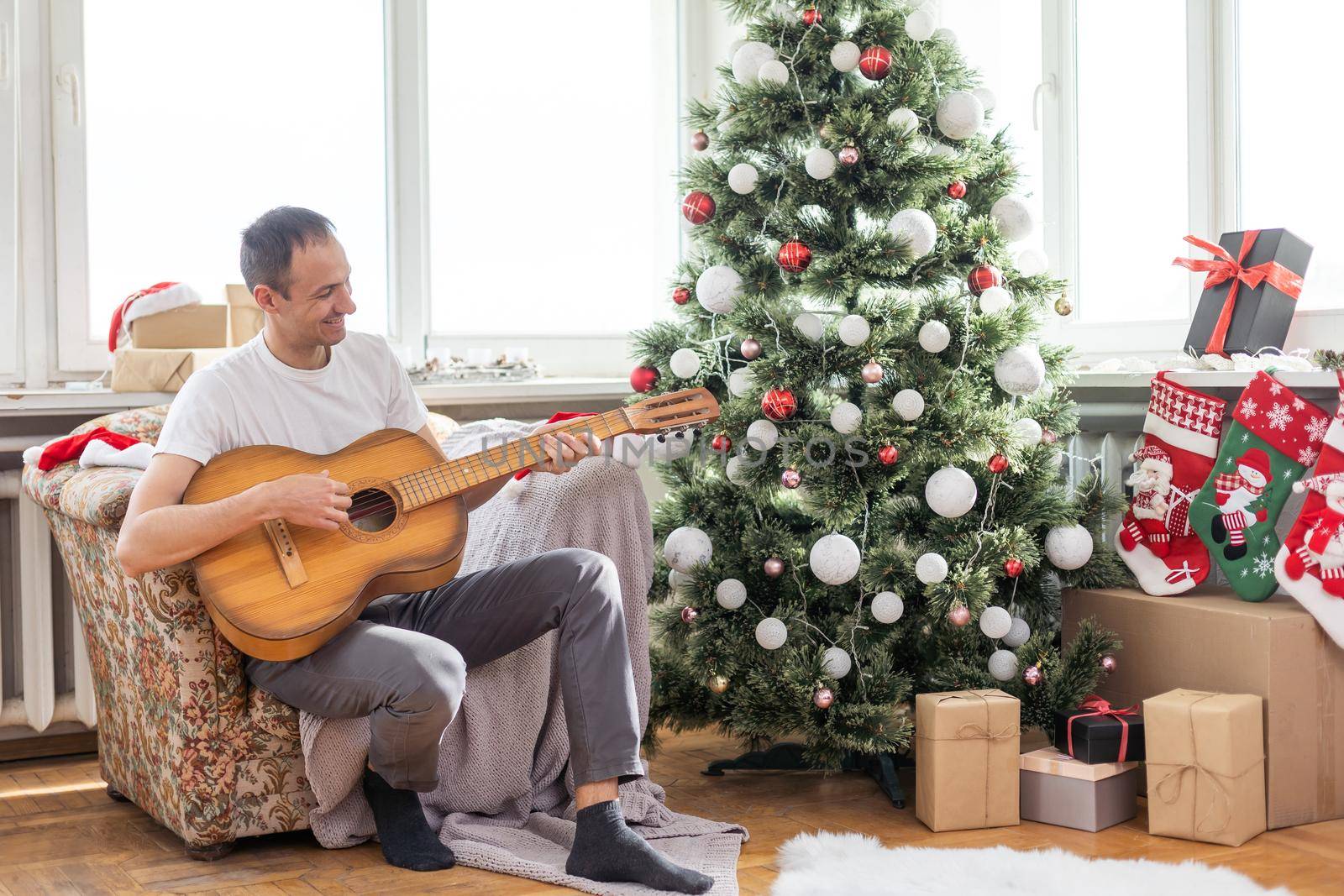 young handsome man sitting on the sofa, he is playing guitar, music, christmas, relax concept by Andelov13
