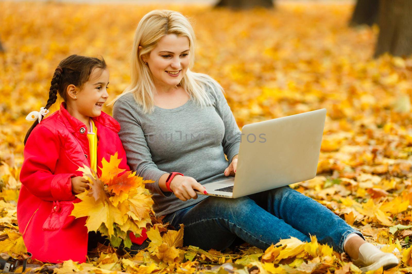 mother and daughter work on laptop outside in autumn. by Andelov13
