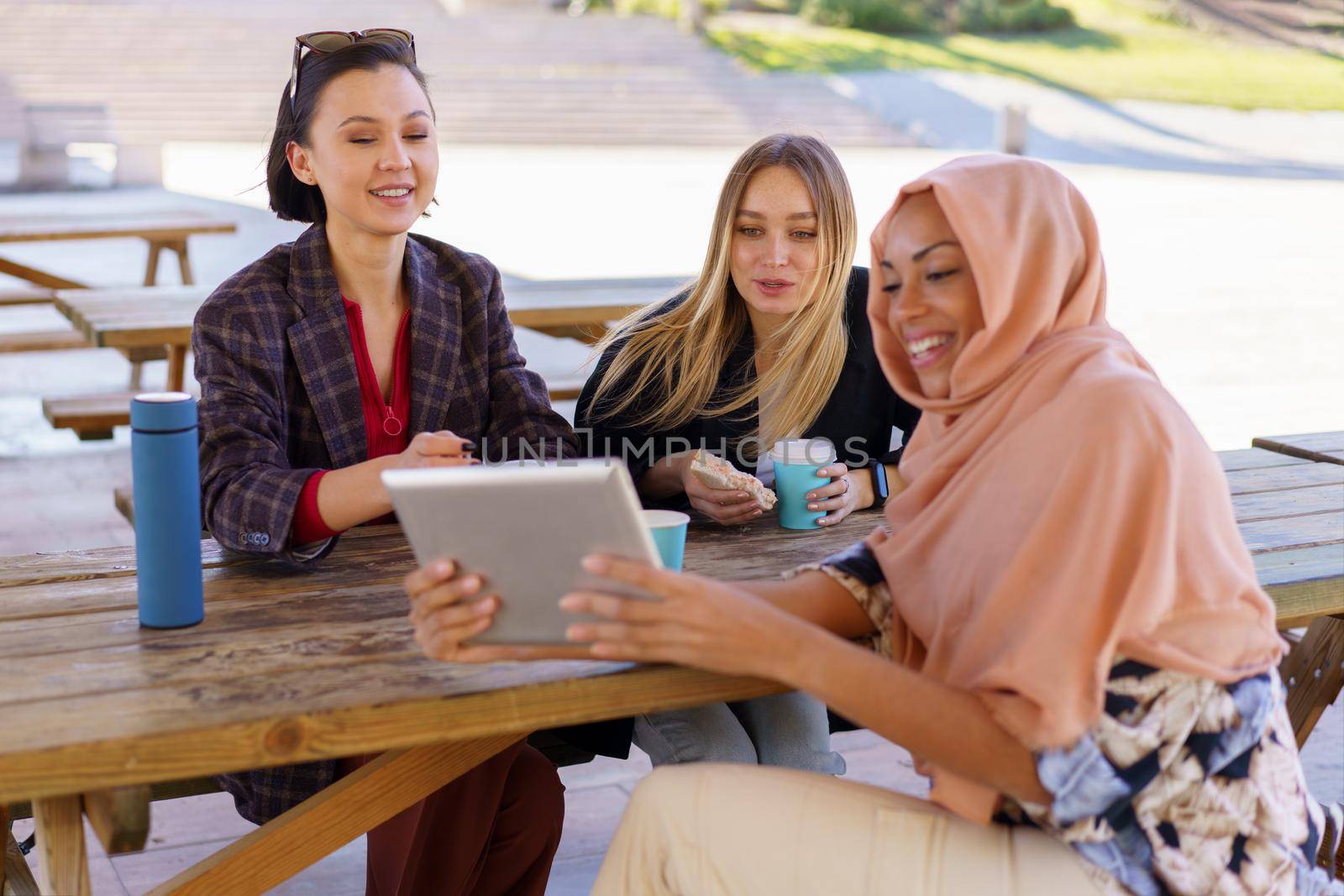 Cheerful diverse women sharing tablet during coffee break in cafe by javiindy