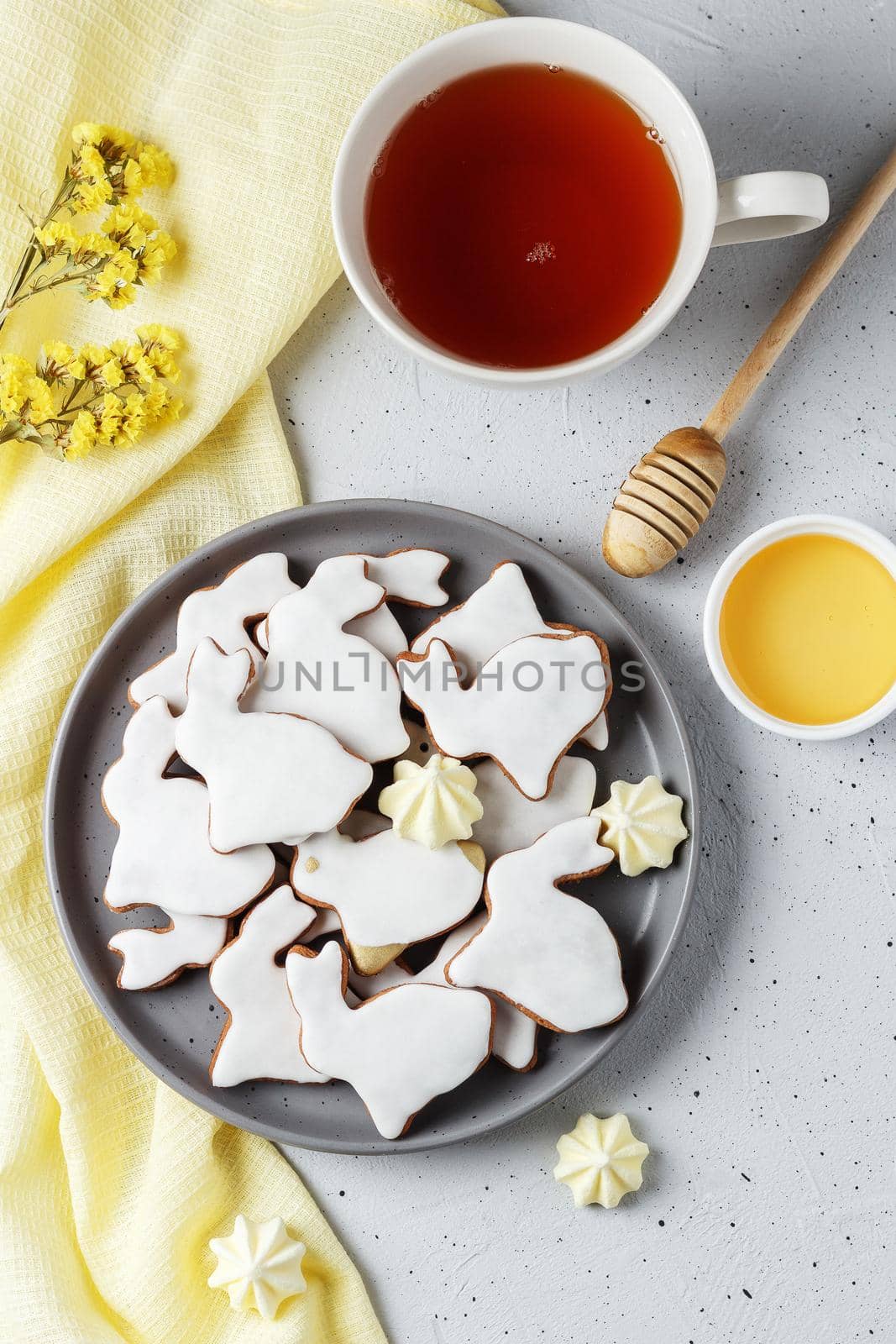 Easter cookies in the form of a rabbit on a gray plate with yellow textiles, a cup of tea and honey on a gray background. vertical photo