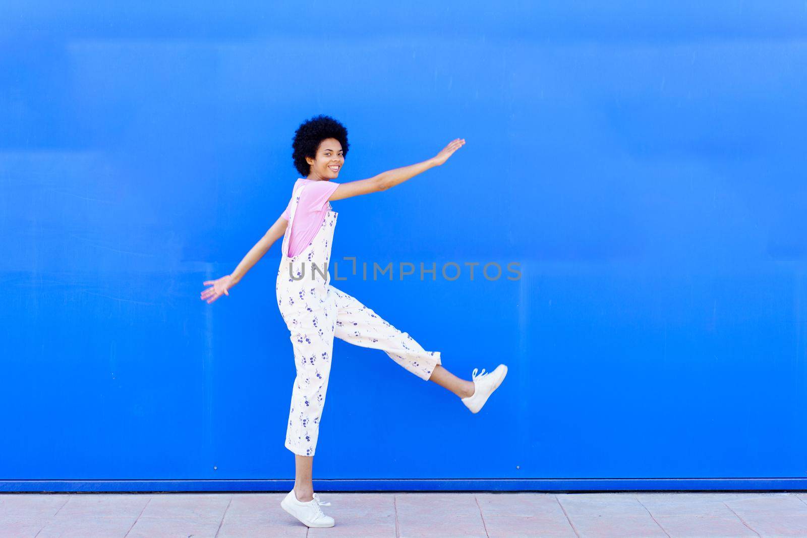 Cheerful black woman raising leg near wall by javiindy