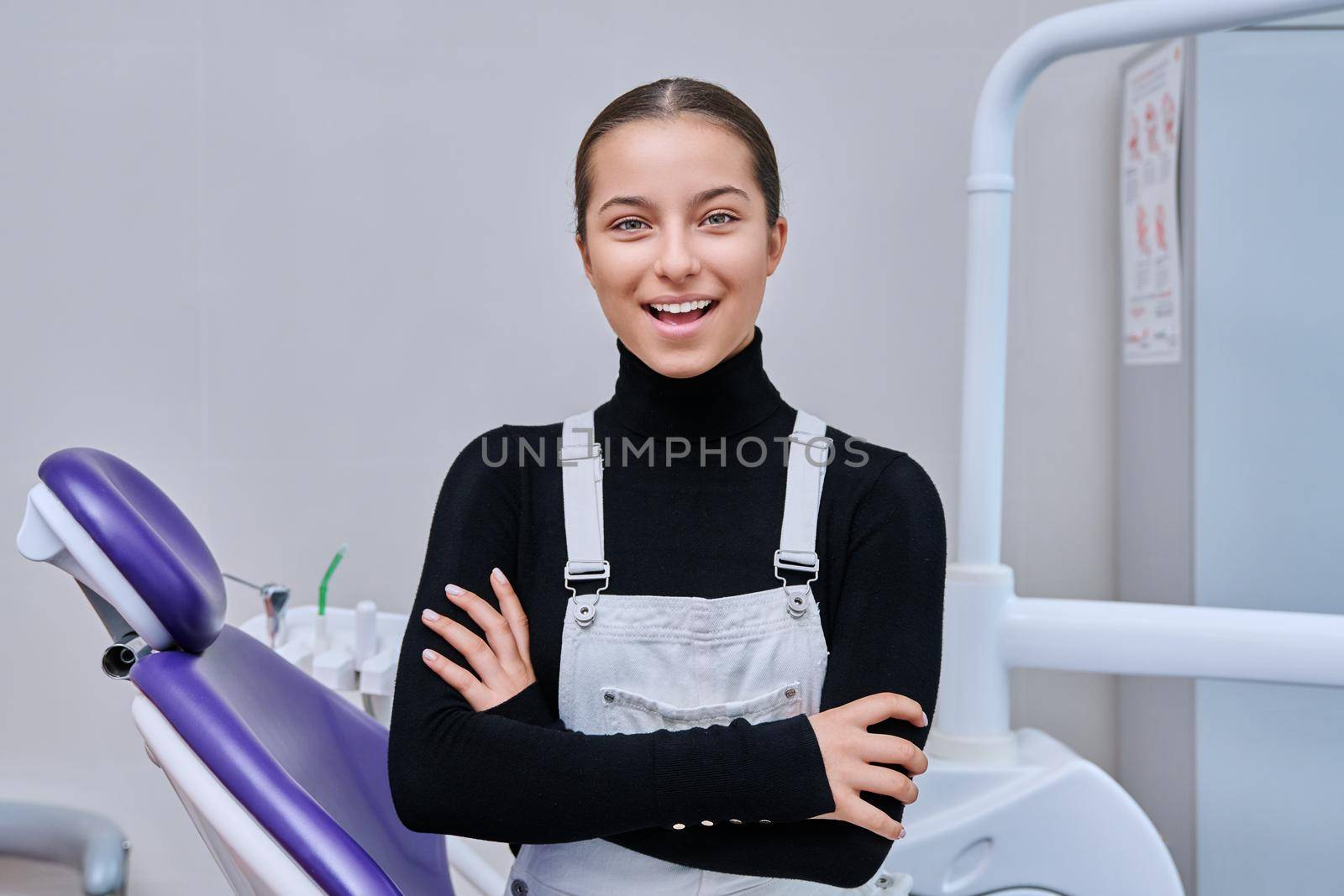 Portrait of young smiling teenage girl in dental chair looking at camera by VH-studio