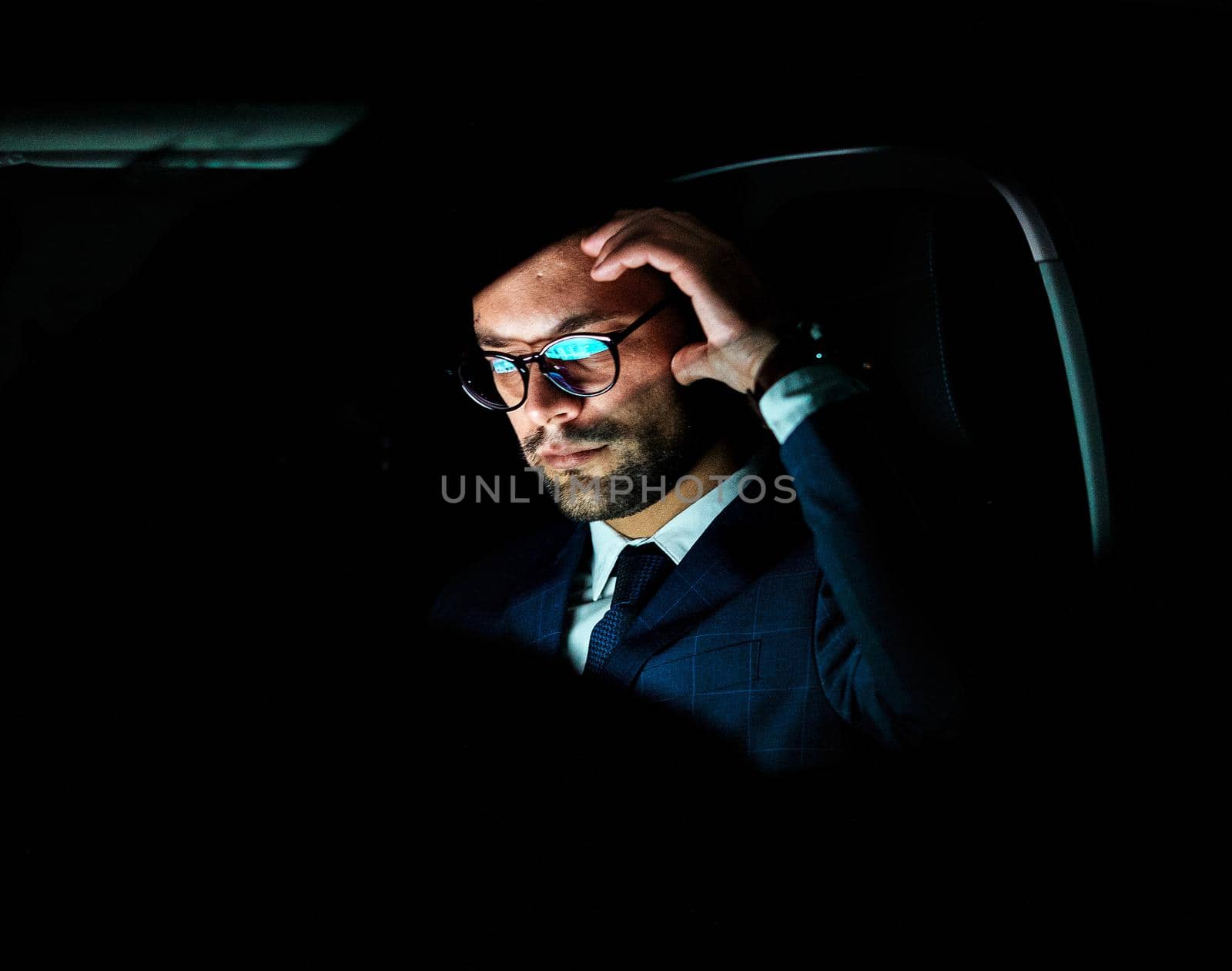 Portrait of a young businessman with tablet or laptop working late at night in office or looking at a device screen in car