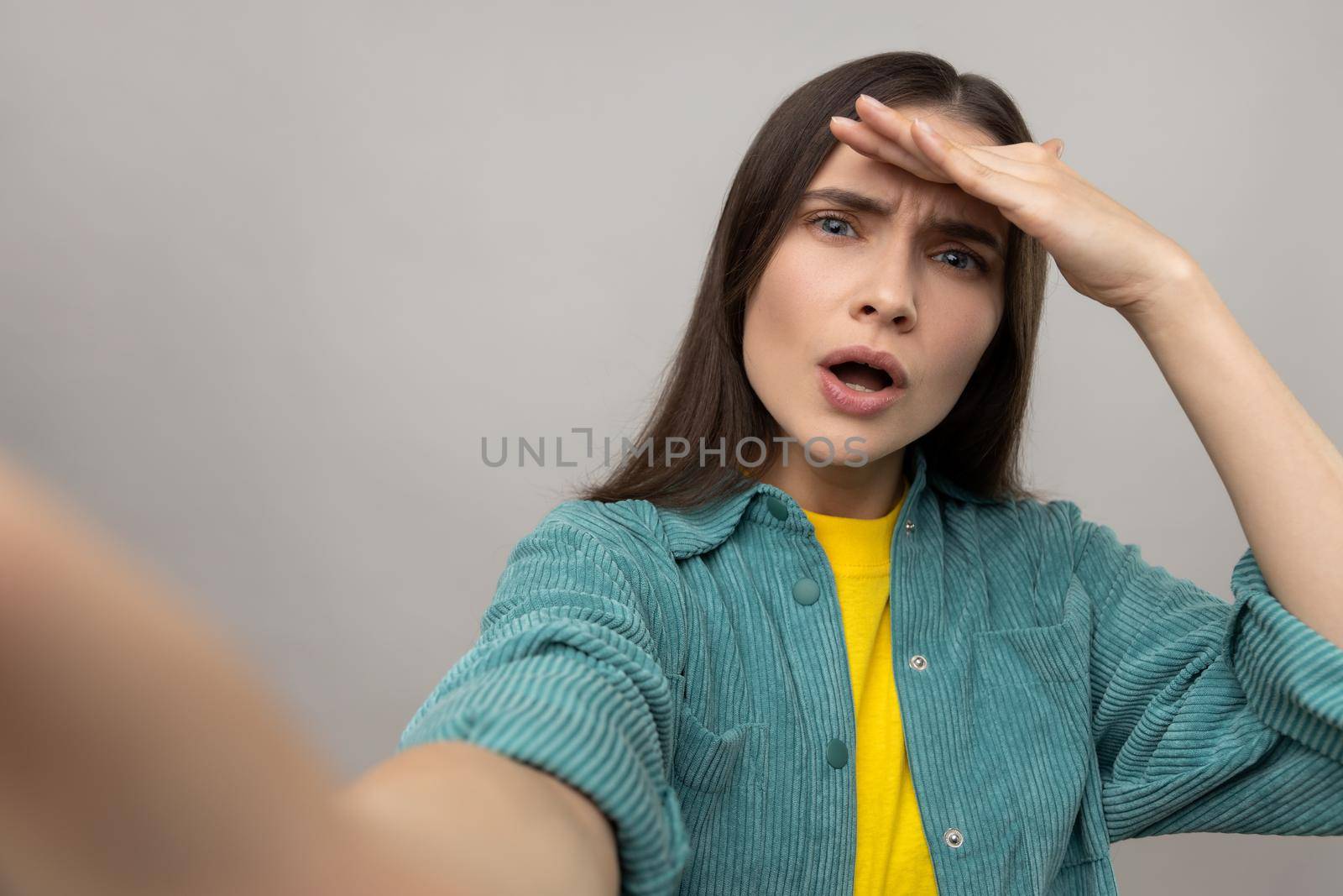 Portrait of astonished woman with amazed face expression, making selfie, looking far away, point of view photo, wearing casual style jacket. Indoor studio shot isolated on gray background.