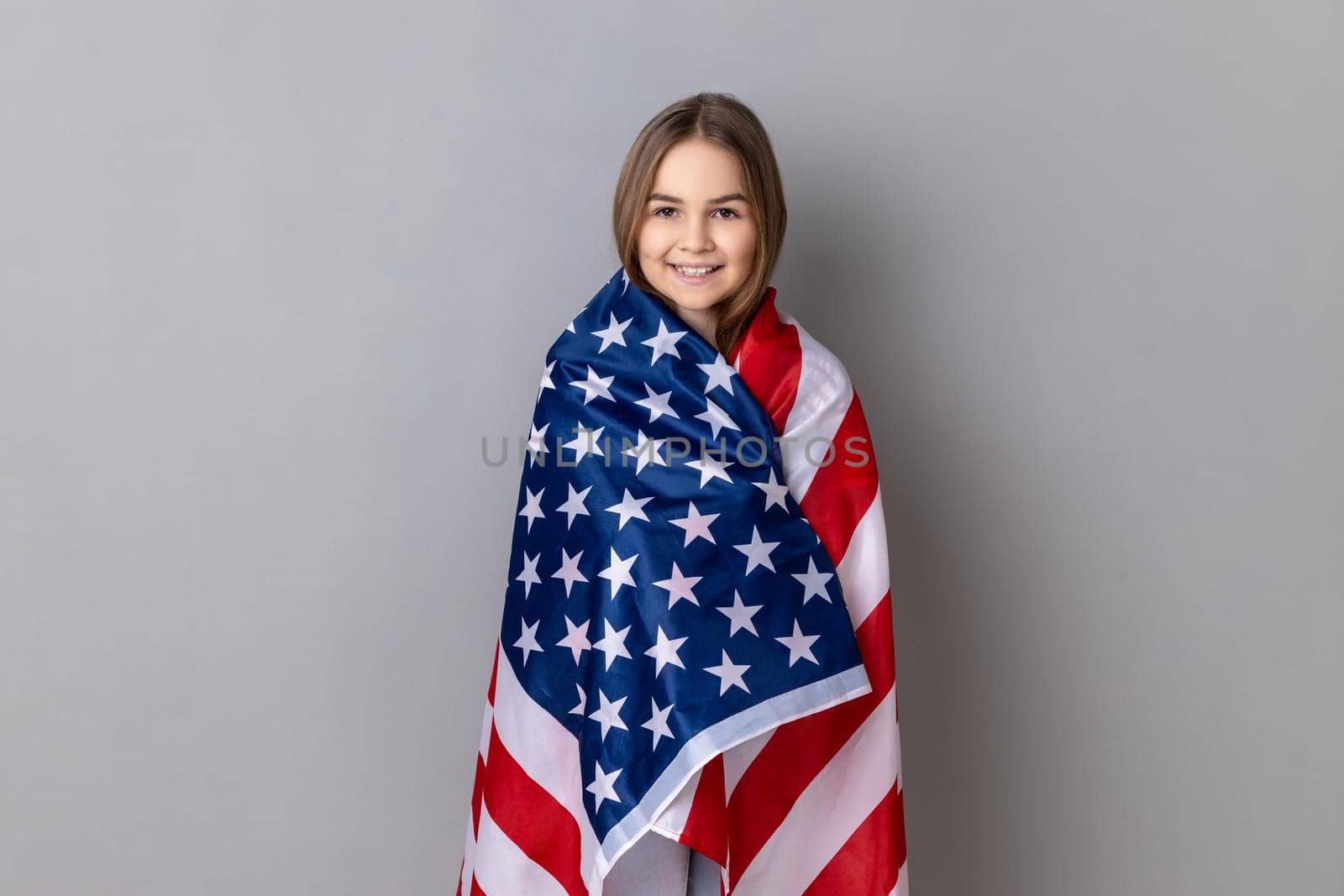 Patriotic little girl standing wrapped in american flag, looking at camera, relocating to America. by Khosro1