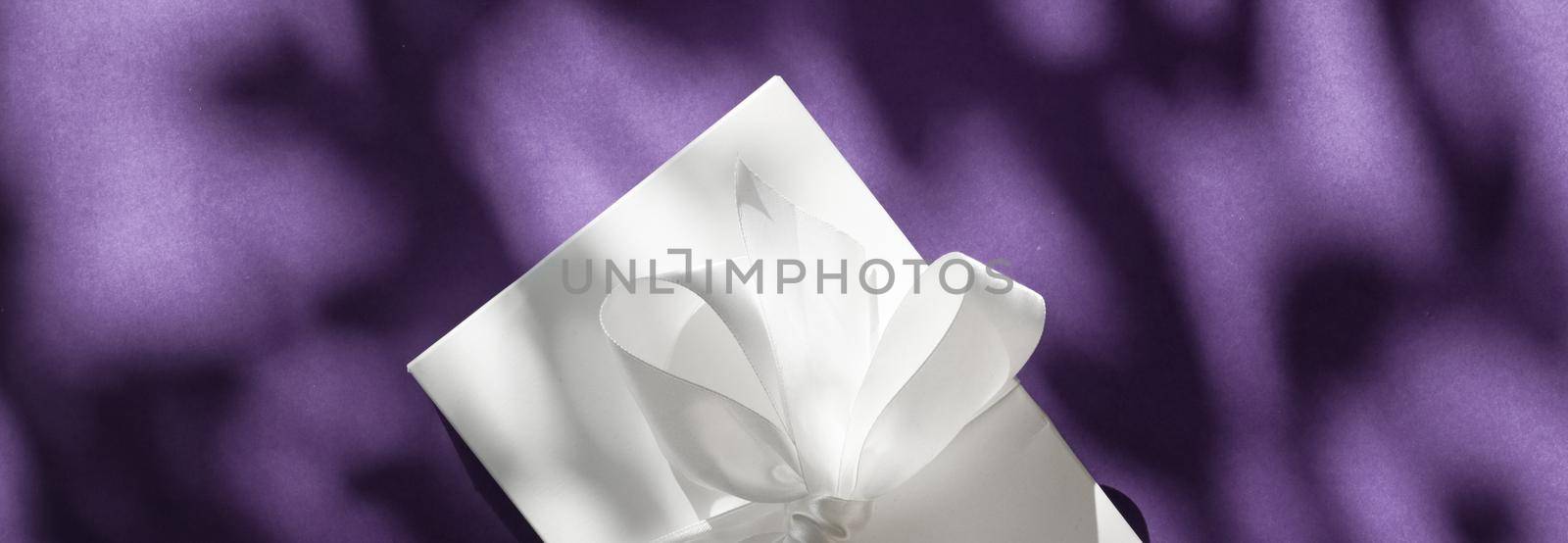 Luxury holiday white gift box with silk ribbon and bow on violet background, luxe wedding or birthday present by Anneleven