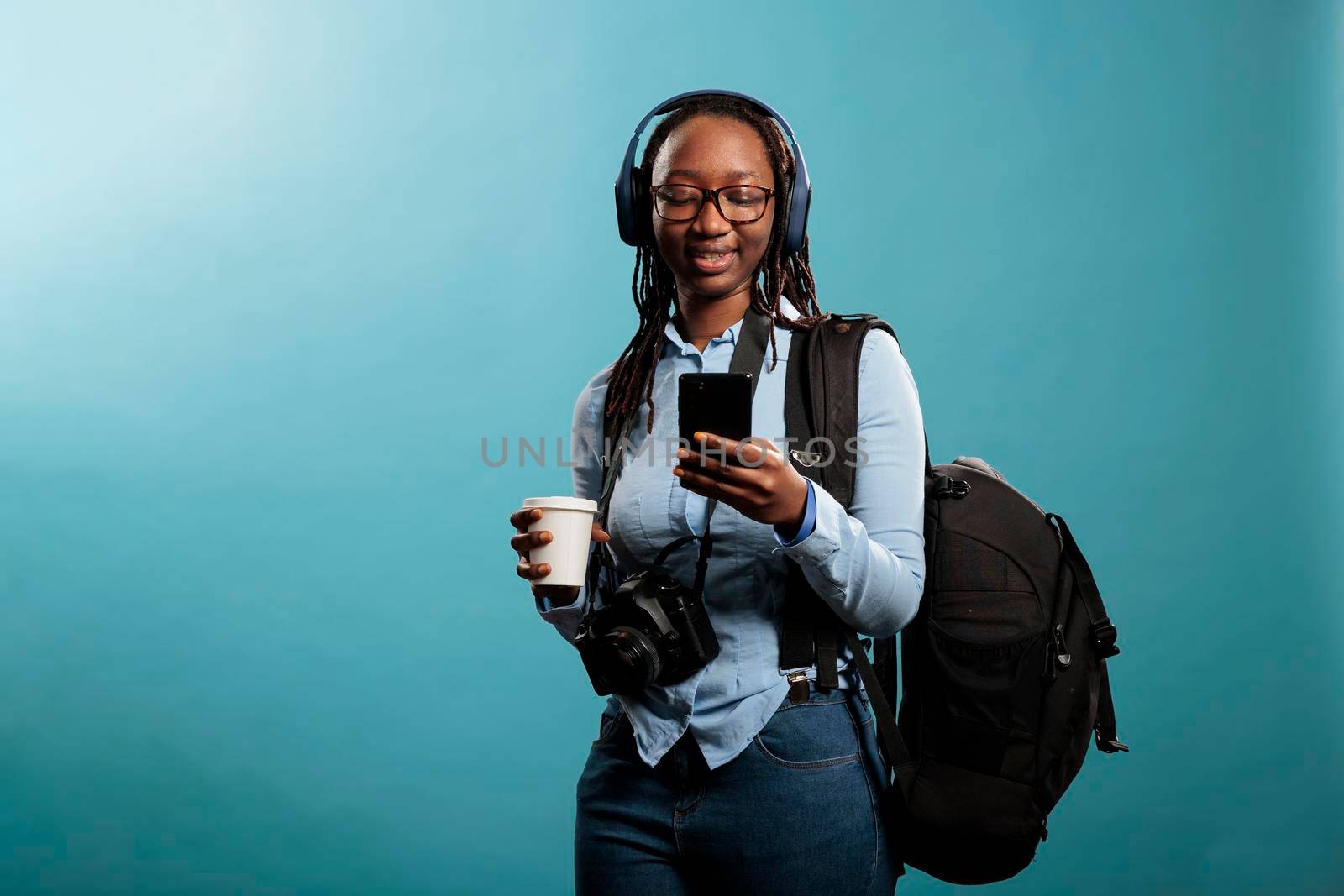 Optimistic professional photographer with smartphone device, wireless headphones and DLSR camera listening to music. Photography entusiast with modern equipment using phone to browse internet.