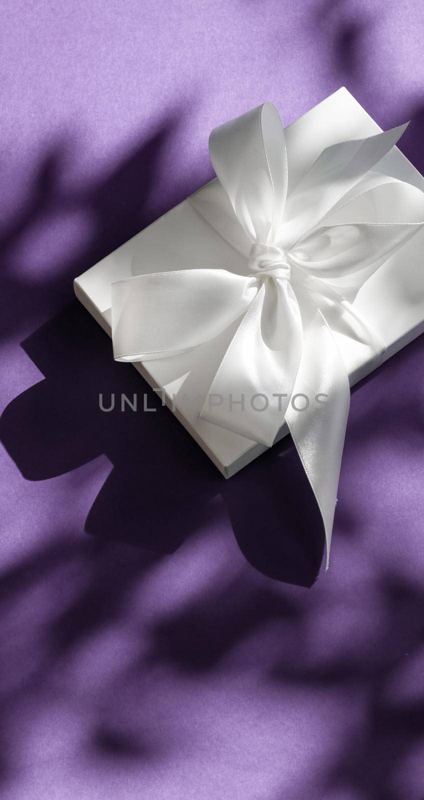 Luxury holiday white gift box with silk ribbon and bow on violet background, luxe wedding or birthday present by Anneleven