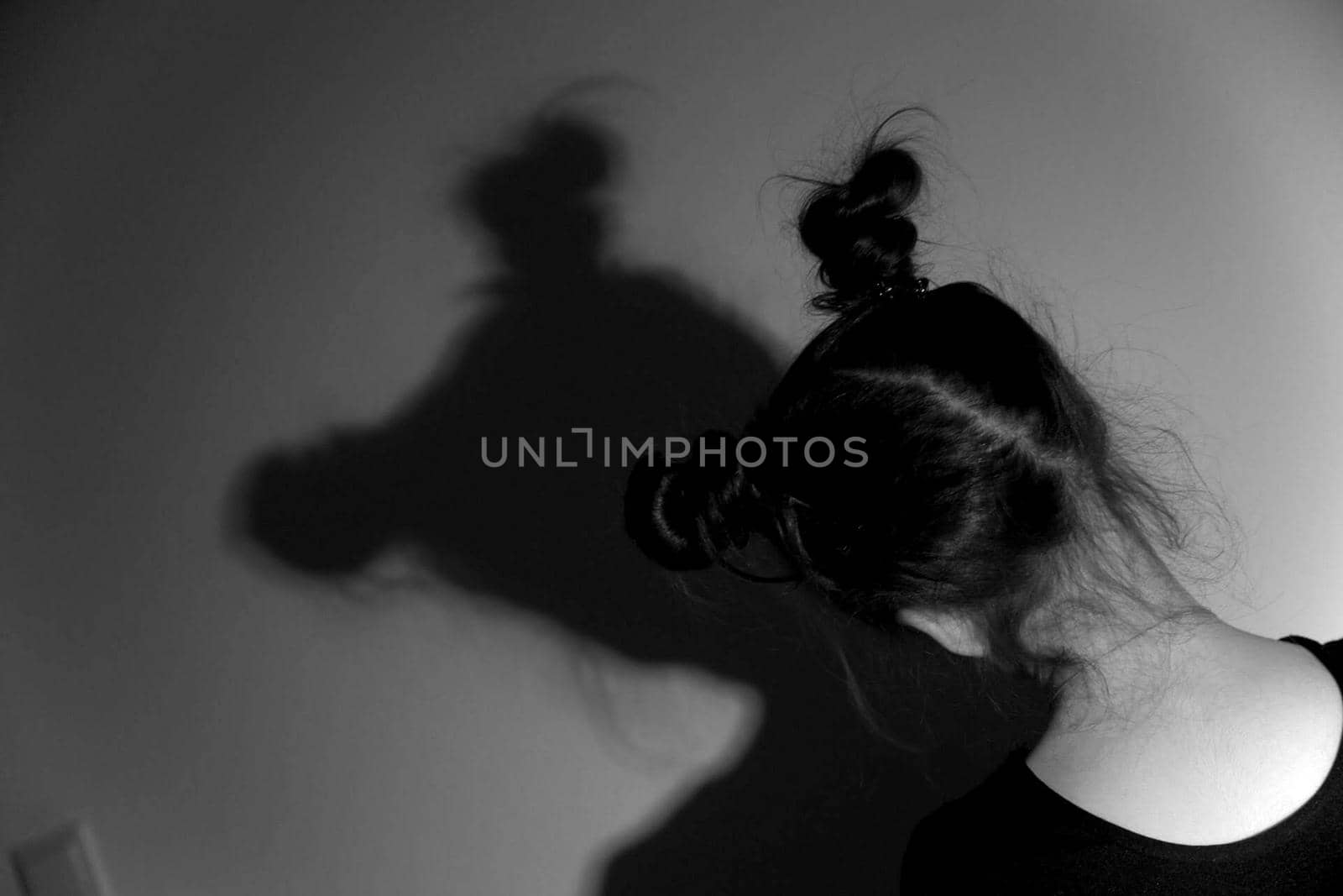 a child's dark-haired head with pigtails is facing the wall on which her shadow is depicted in a black-and-white photo by Costin