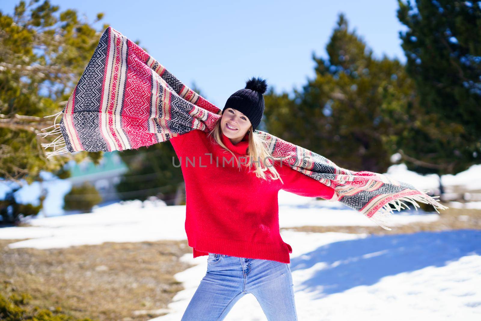 Happy young blonde woman waving her scarf in the wind in a forest in the snowy mountains in Sierra Nevada, Granada, Andalusia, Spain