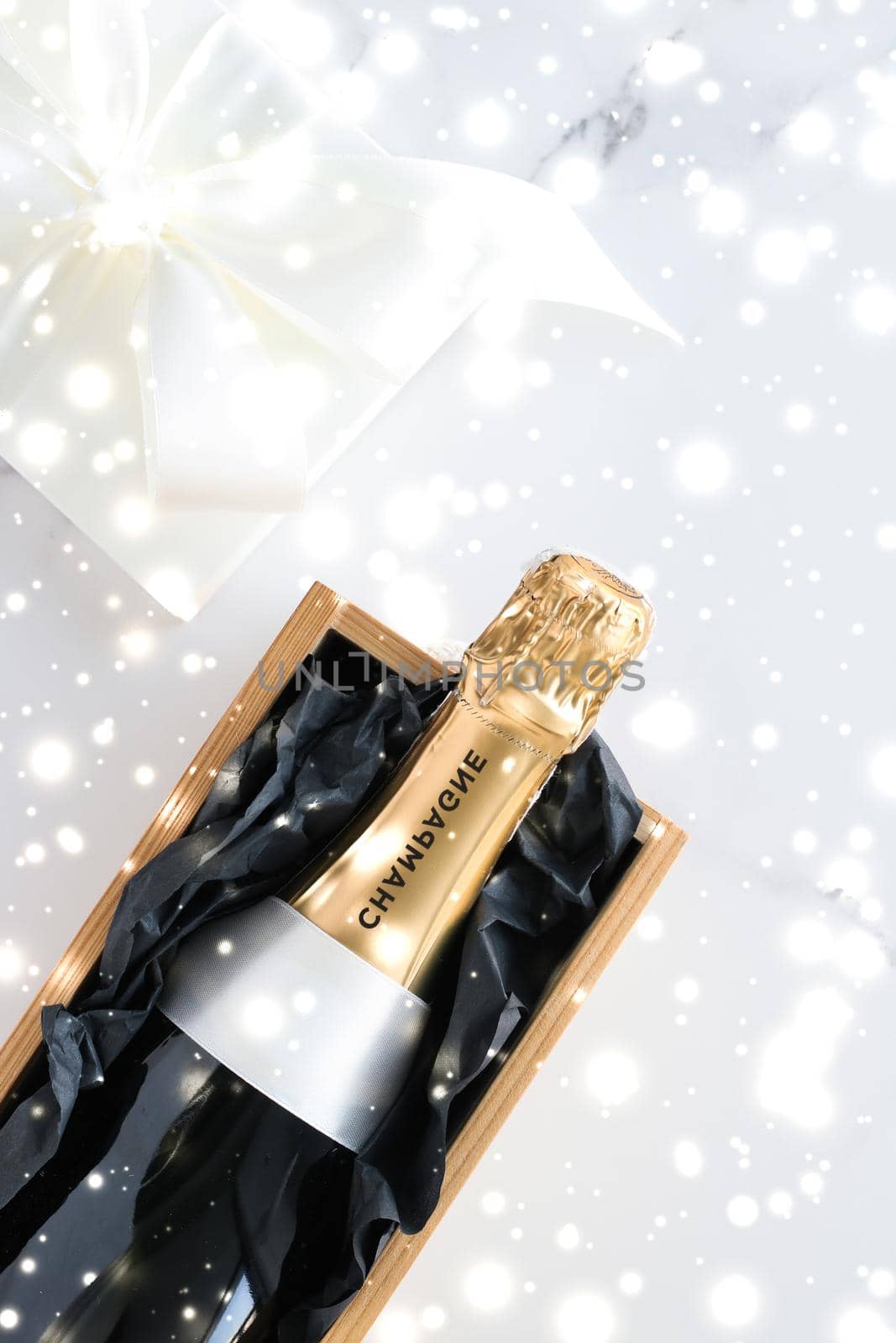 Christmas holiday champagne bottle and a gift box and shiny snow on marble background by Anneleven