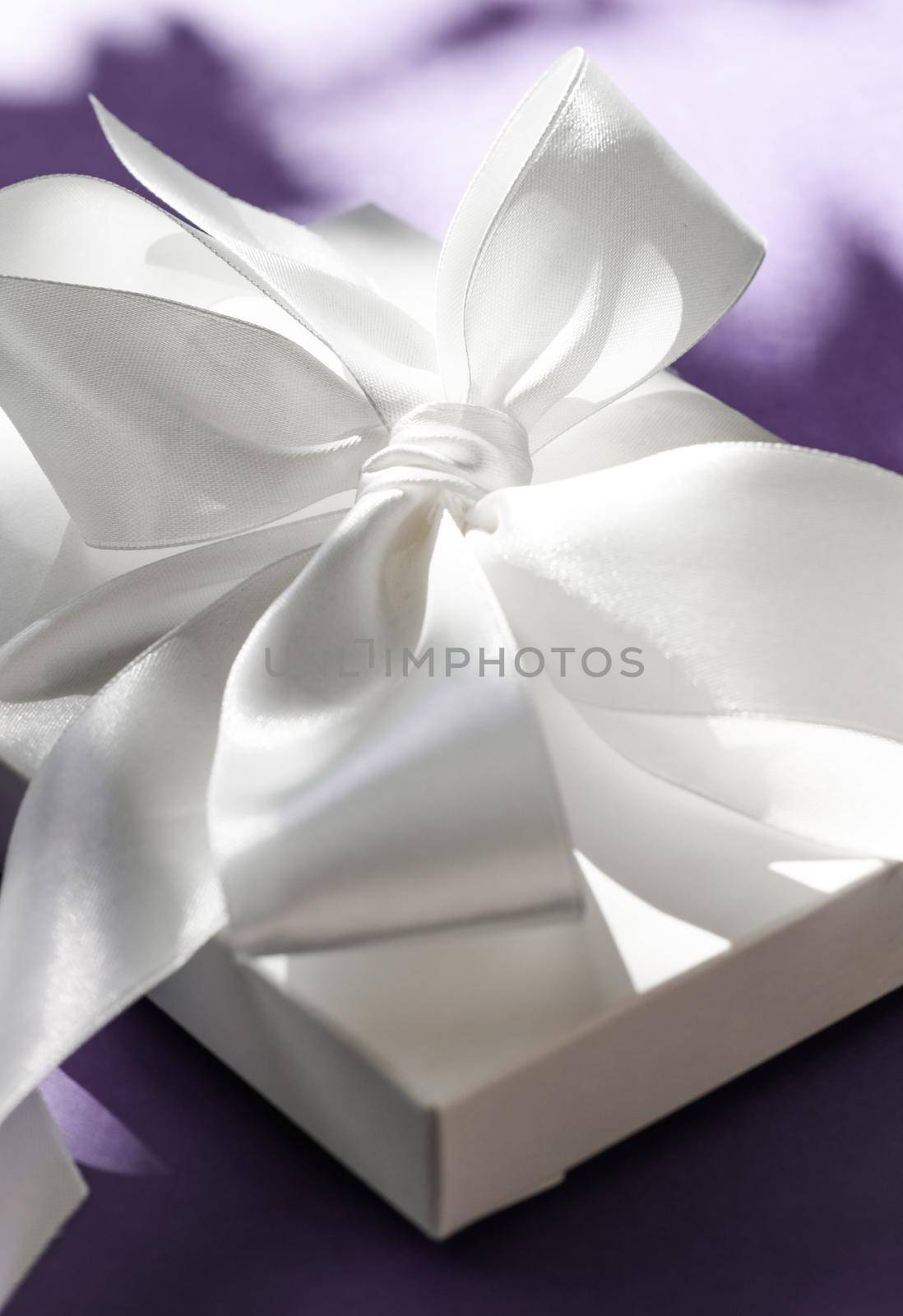 Anniversary celebration, shop sale promotion and bridal surprise concept - Luxury holiday white gift box with silk ribbon and bow on violet background, luxe wedding or birthday present
