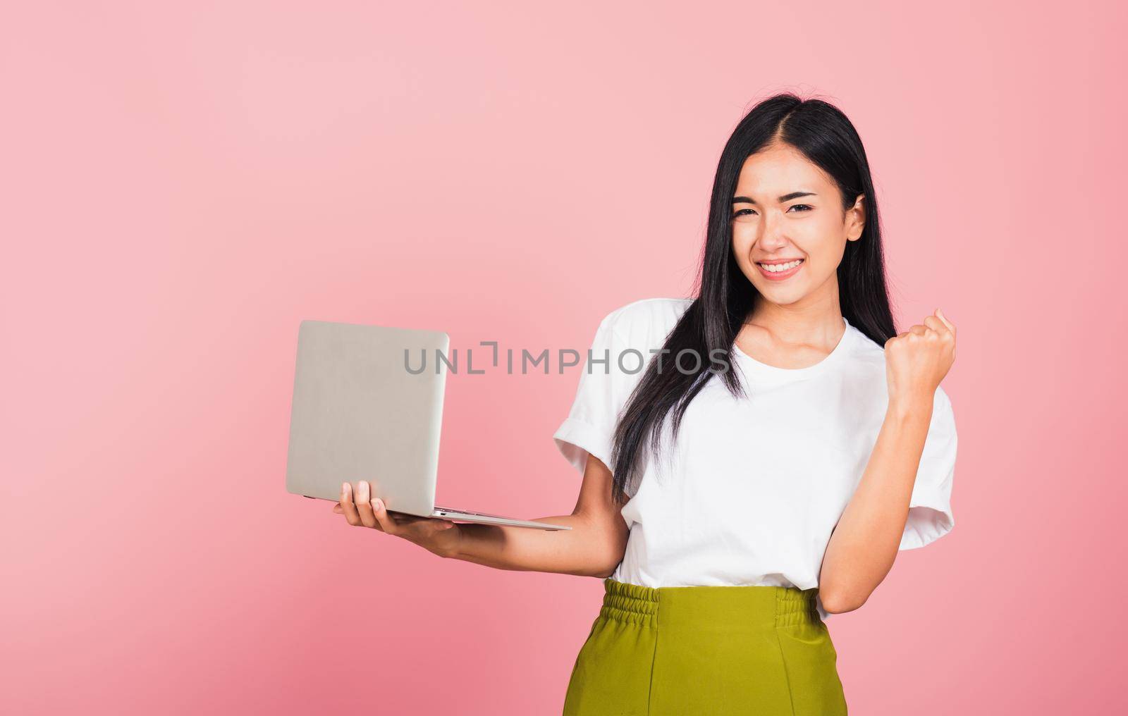 Portrait of happy Asian beautiful young woman teen confident smiling face holding using laptop computer and excited celebrating success, studio shot isolated on pink background, with copy space