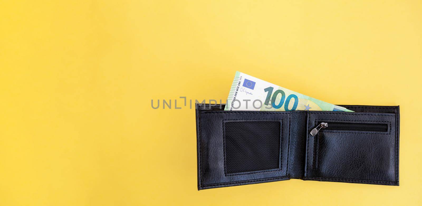 100 euro banknote sticks out of a black wallet on a yellow background by AnatoliiFoto