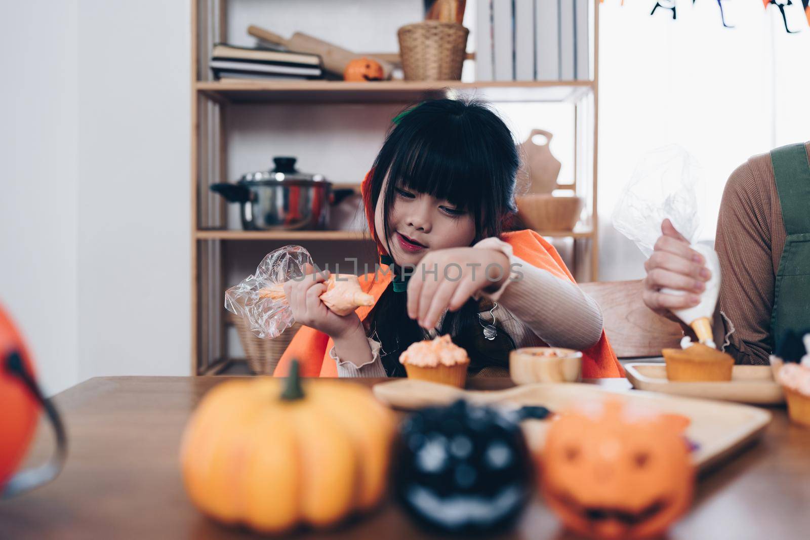 Young girl and mother at Halloween making treats and cupcake on table. Happy Halloween day.