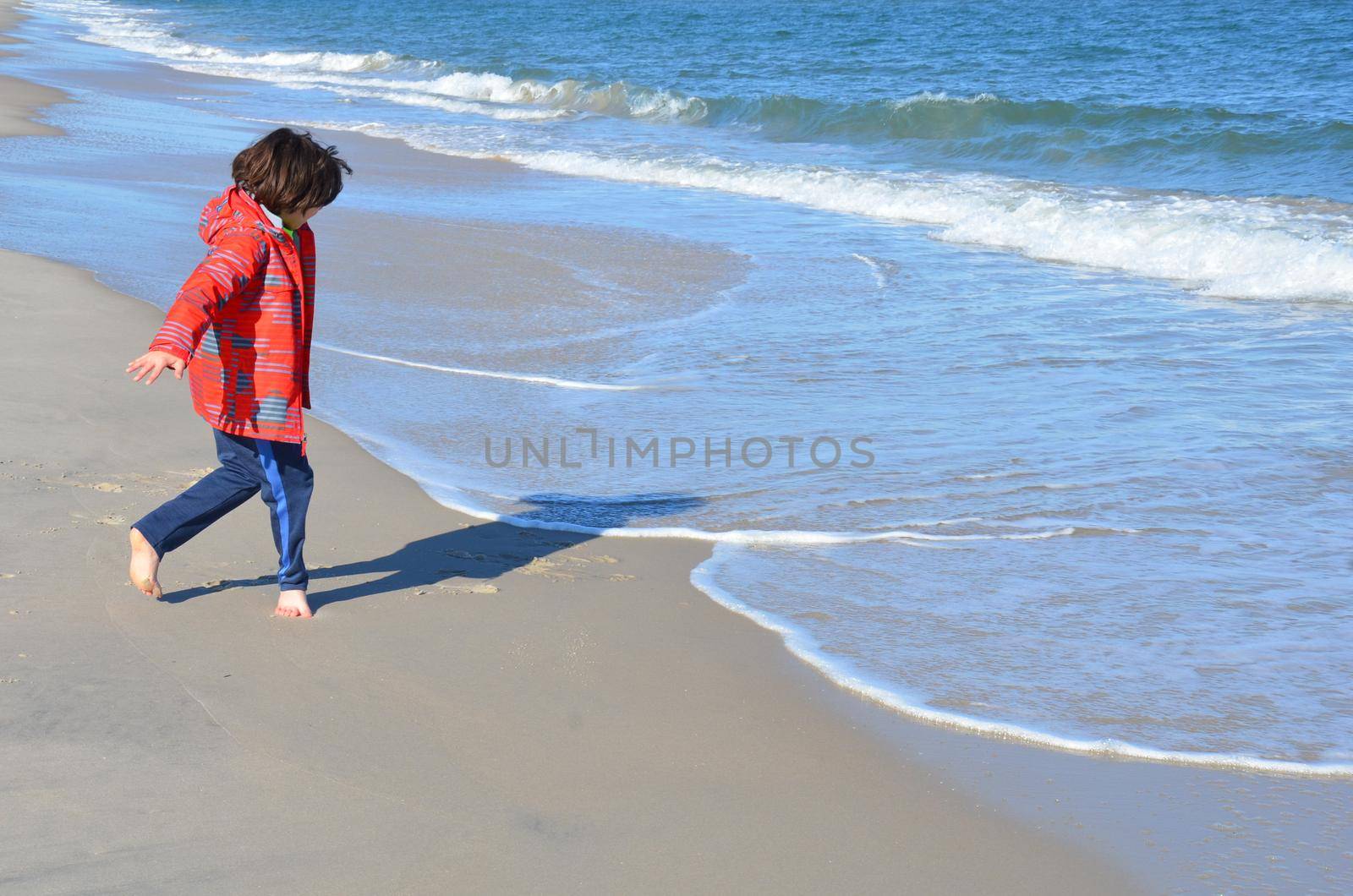boy in red jacket and beach with water and sand and waves