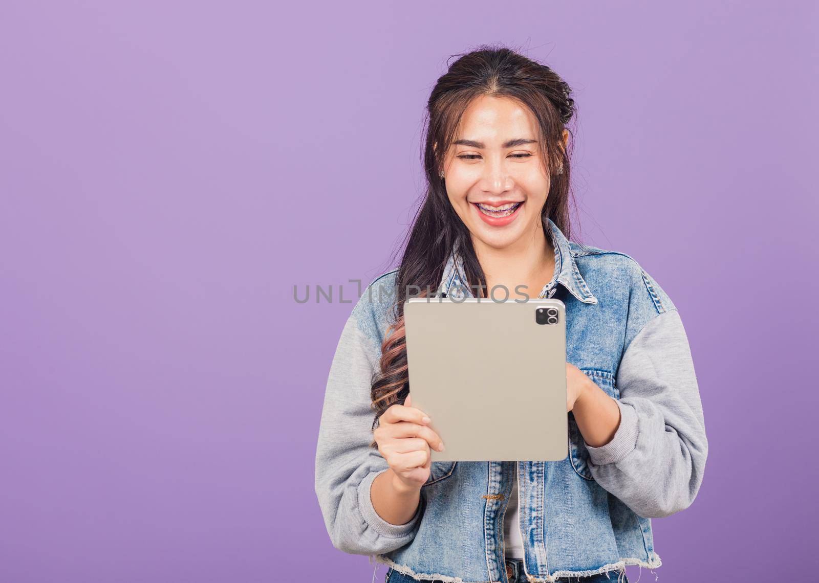 Portrait of Asian beautiful young woman smiling using tablet computer, Happy lifestyle female teen touching screen on digital tablet pc, studio shot isolated on purple background