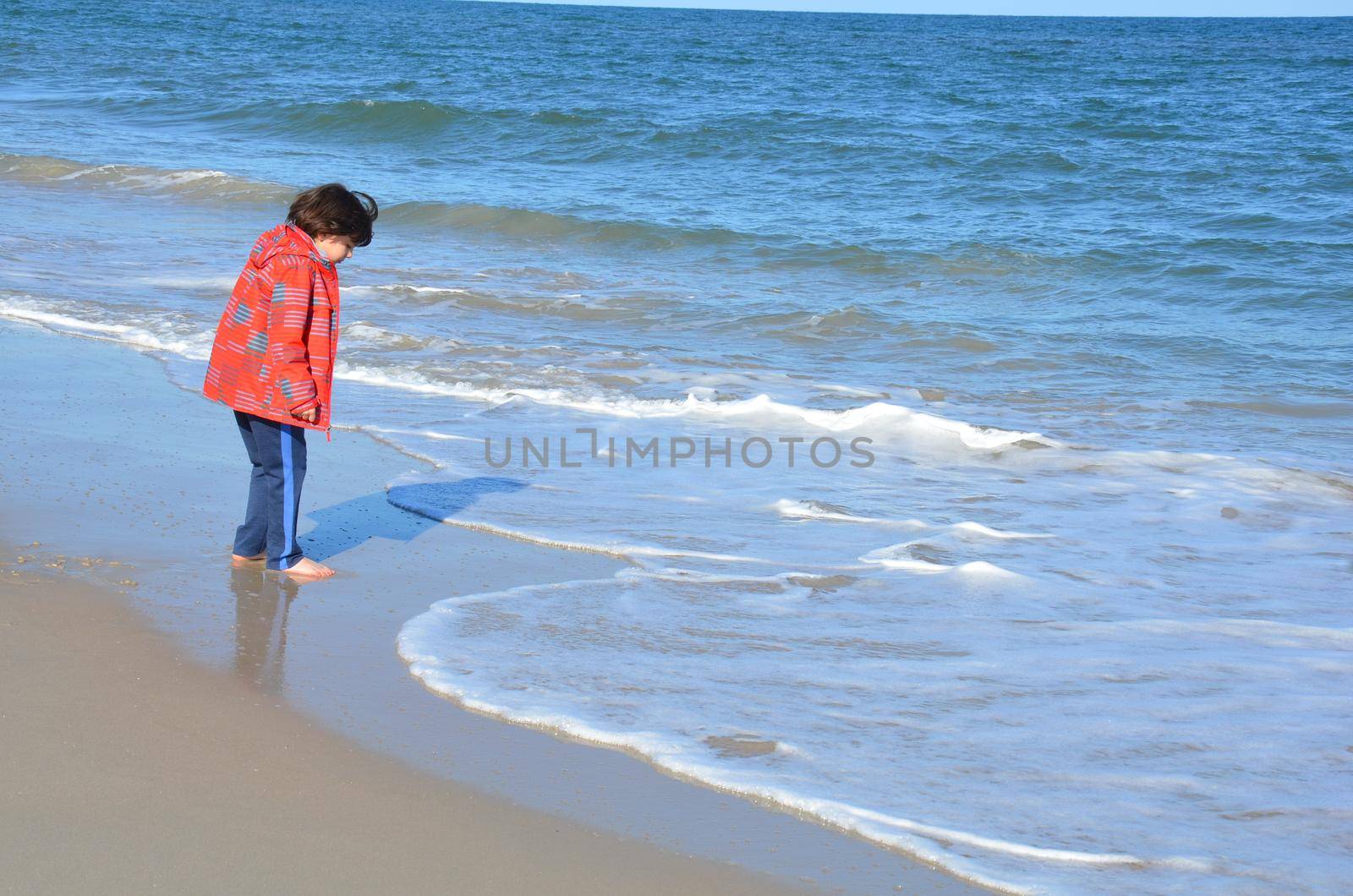 boy in red jacket and beach with water and sand and waves