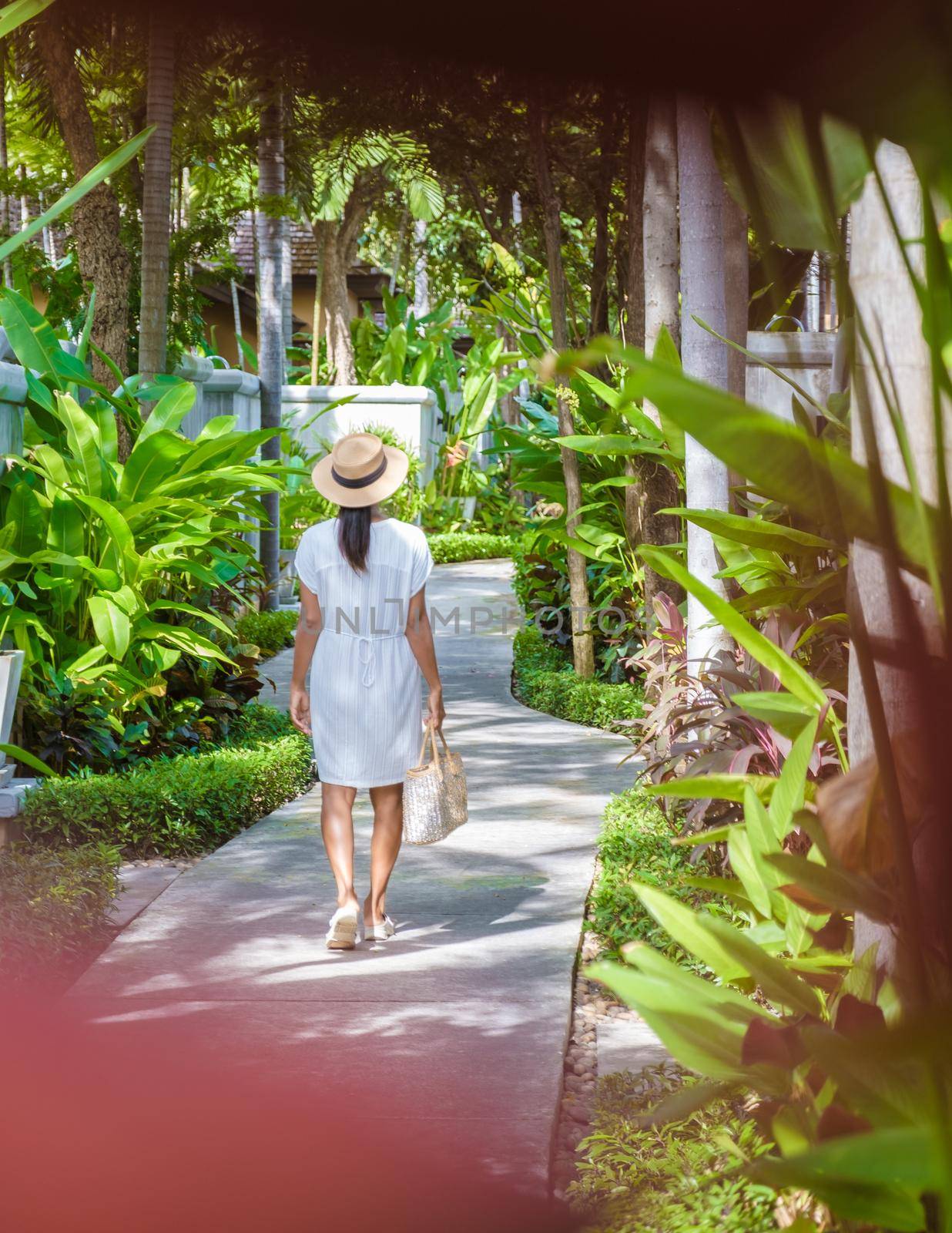 Asian women with a hat walking in a tropical garden during vacation. Young women in a tropical garden