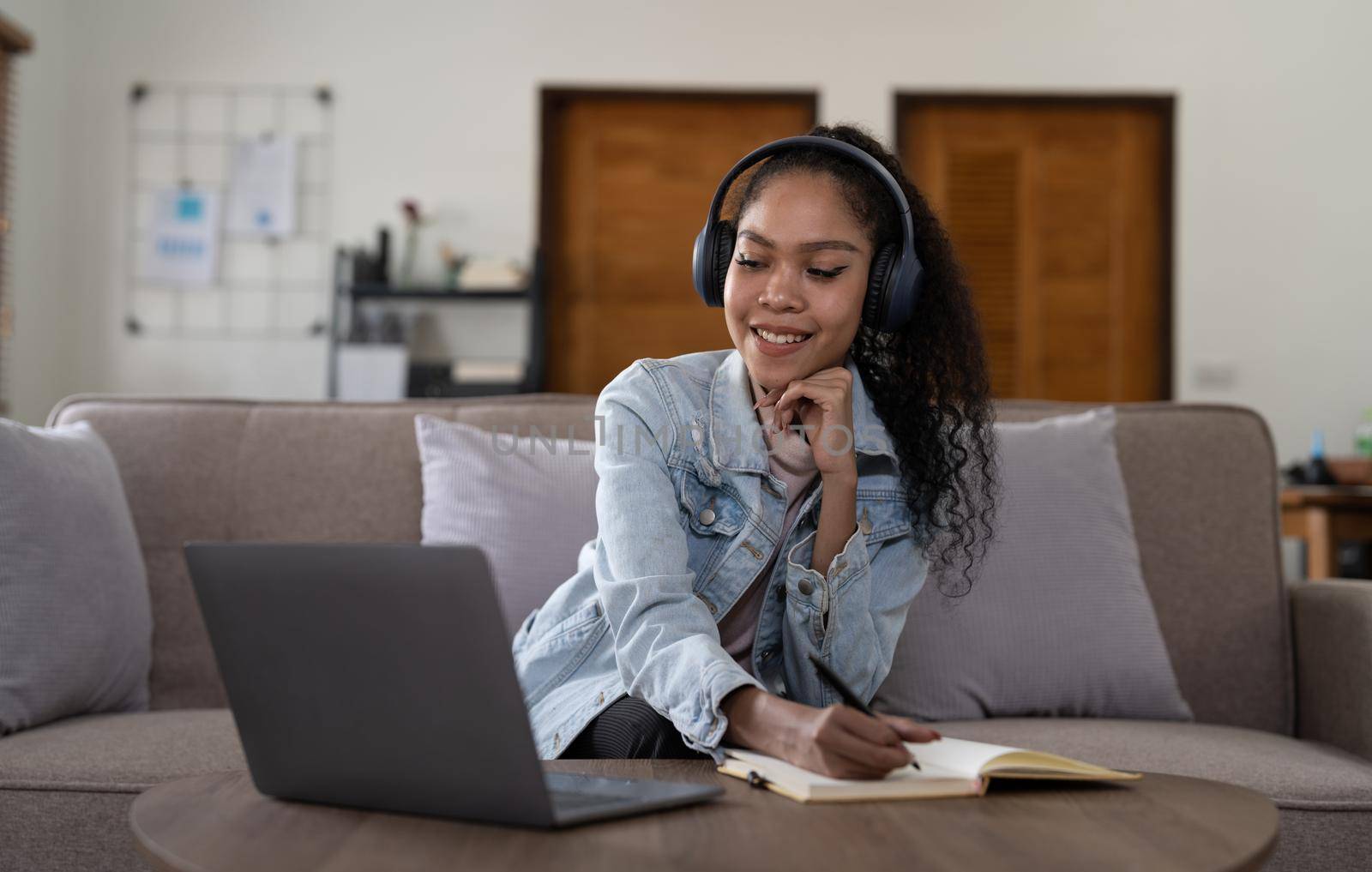 mixed race woman wearing headphones watching webinar write notes study online with online teacher, african female student learning language computer course on laptop listen translate lecture.