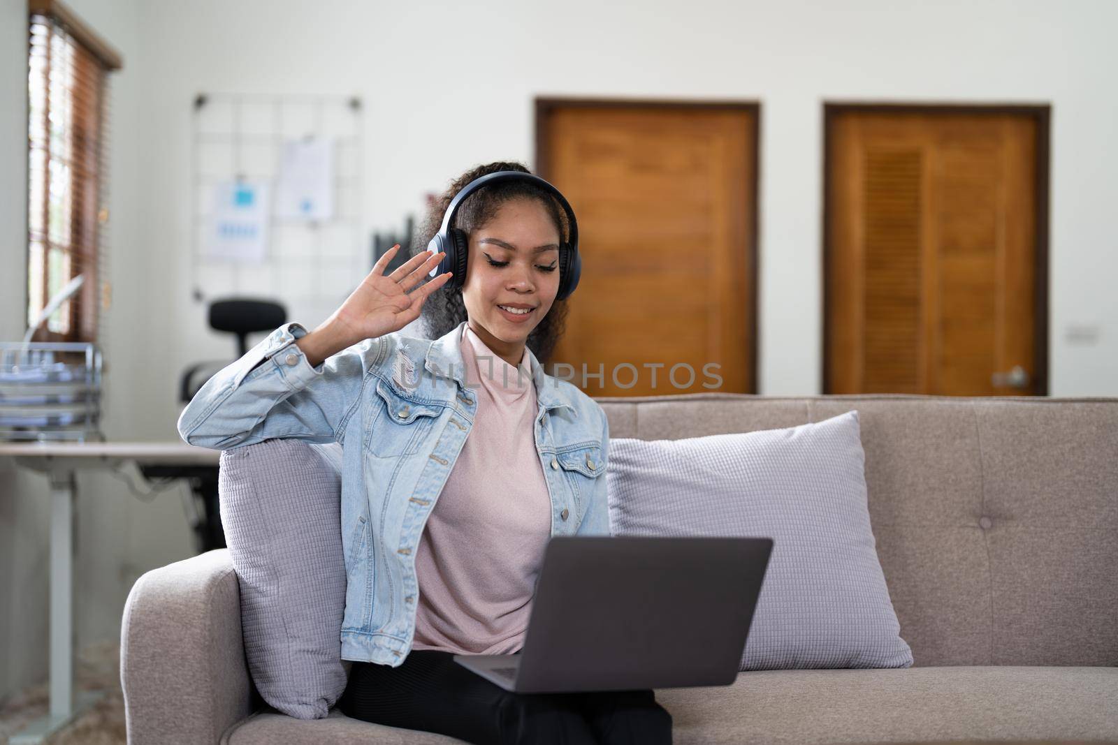 Young woman sitting on sofa at home video call chatting with friends using a laptop at home
