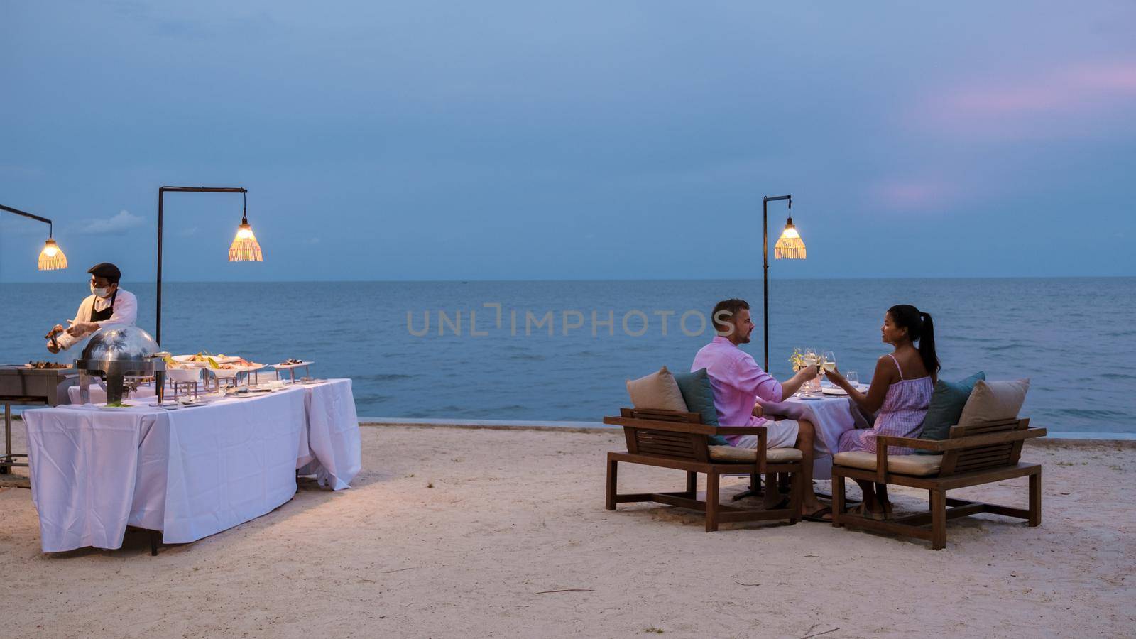 A couple of men and women having a romantic dinner on the beach in the evening. Asian women and Caucasian men having dinner on the beach of Huahin Thailand
