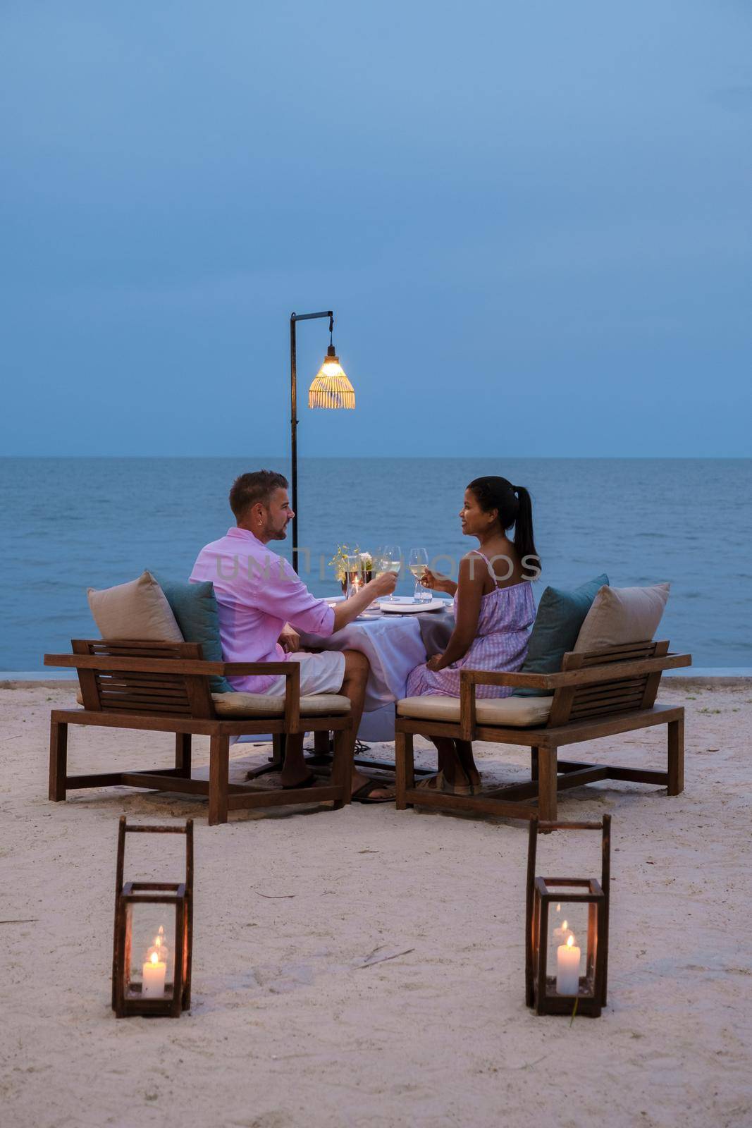 Couple men and women having a romantic dinner on the beach in the evening by fokkebok