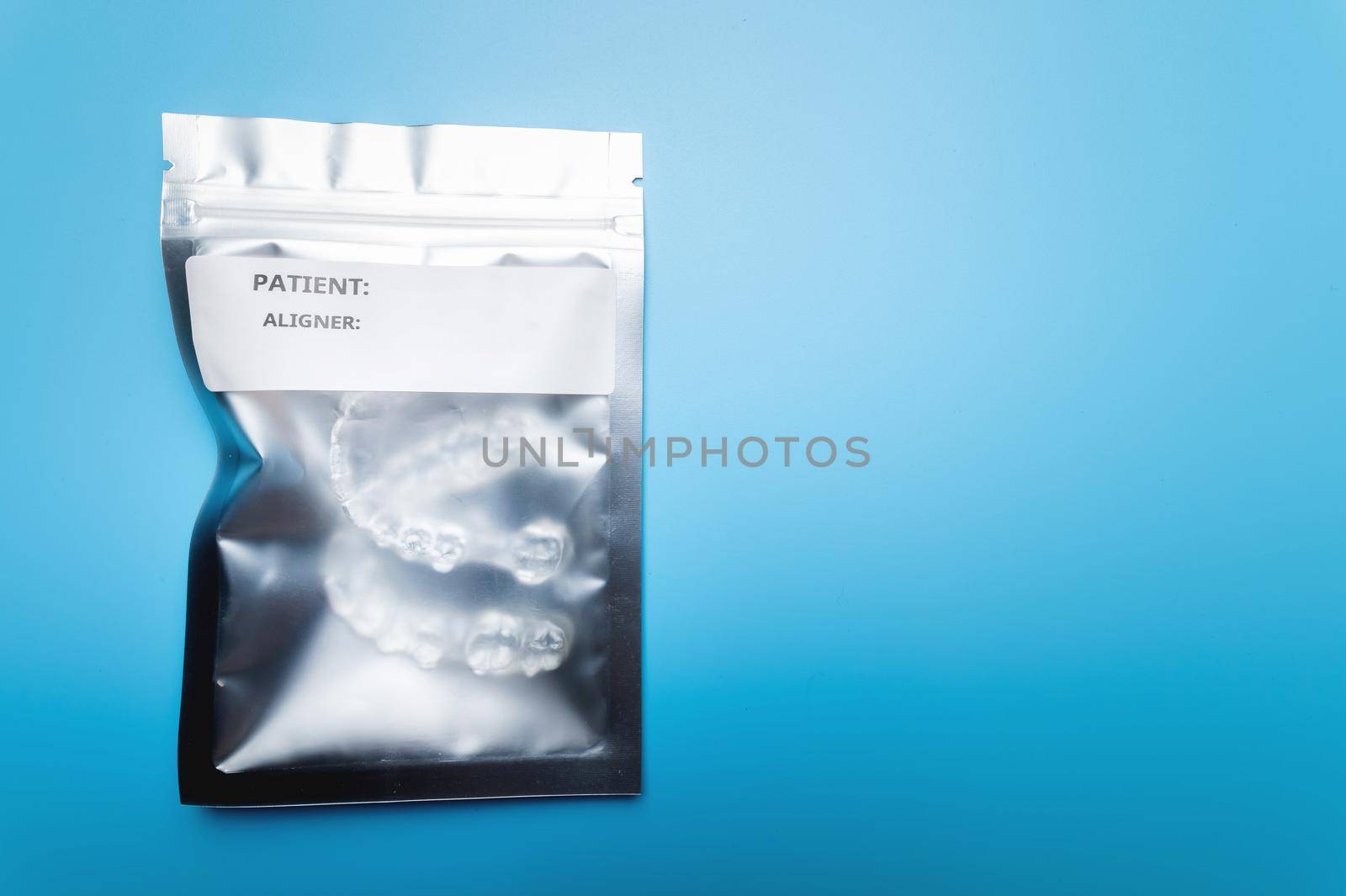 Silver plastic bag with a zip closure with transparent braces on a blue background. Invisible removable retainers for orthodontic treatment by yanik88