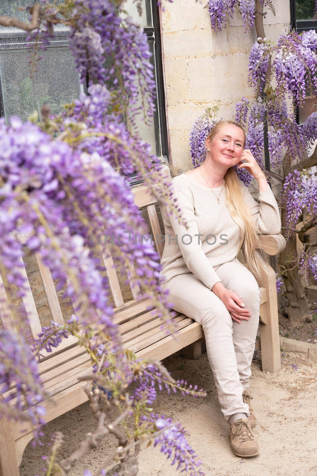 a beautiful middle-aged woman sits on a bench in the thickets of blooming wisteria and meditates happy. High quality photo