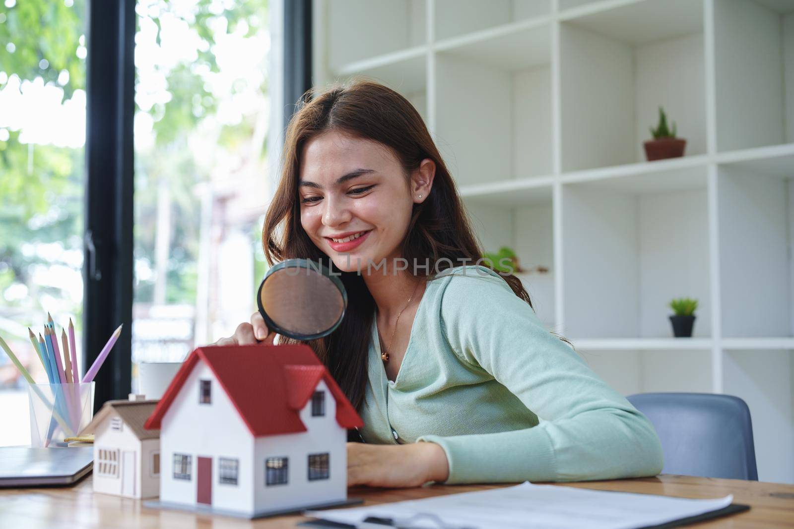 The client holds a magnifying glass to select a house model, inspect the concept of a home before making a decision to invest, make a loan, get insurance and sign important documents with the bank