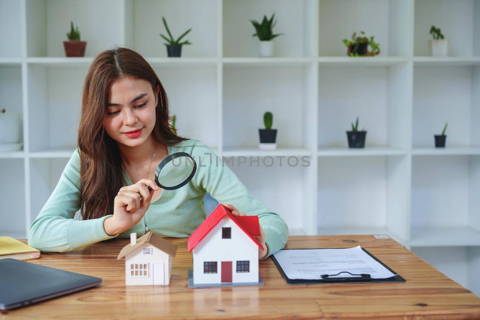 The client holds a magnifying glass to select a house model, inspect the concept of a home before making a decision to invest, make a loan, get insurance and sign important documents with the bank