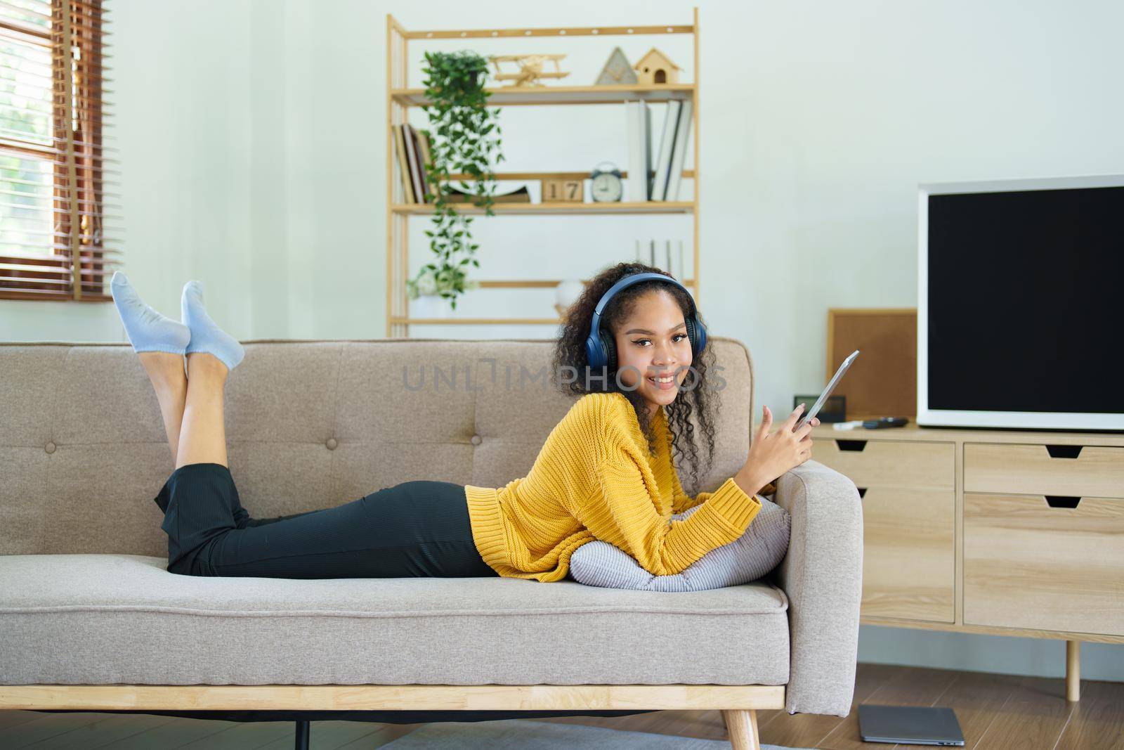 Portrait of an African American with headphones and tablet smiling happily listen music while relaxing on the sofa at home.