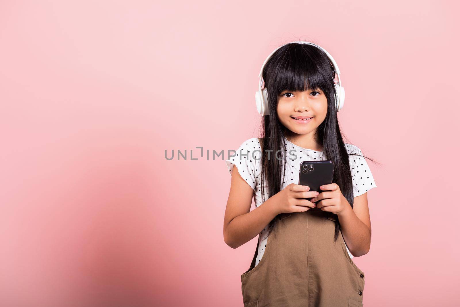Asian kid 10 years enjoying listening music from mobile phone wear wireless headset by Sorapop