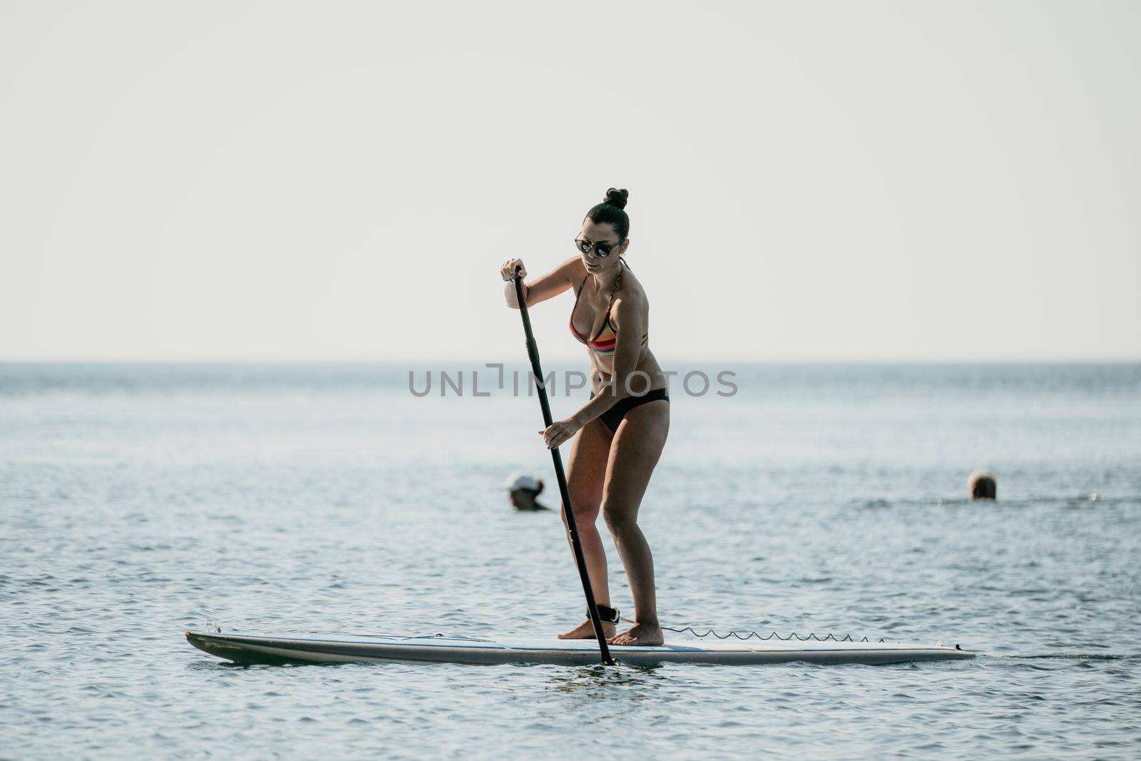 Silhouette of woman standing, surfing on SUP board, confident paddling through water surface. Idyllic sunset or sunrise. Sports active lifestyle at sea or river.