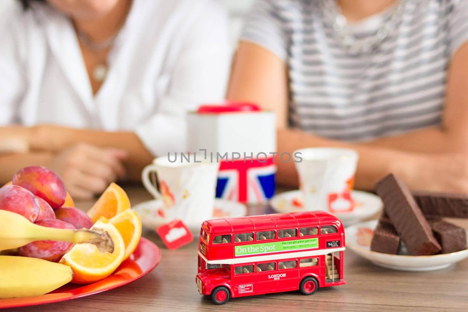 Traditional afternoon tea of british ceremony with such symbol of London as toy double decker bus, defocused faceless women on background, front focus