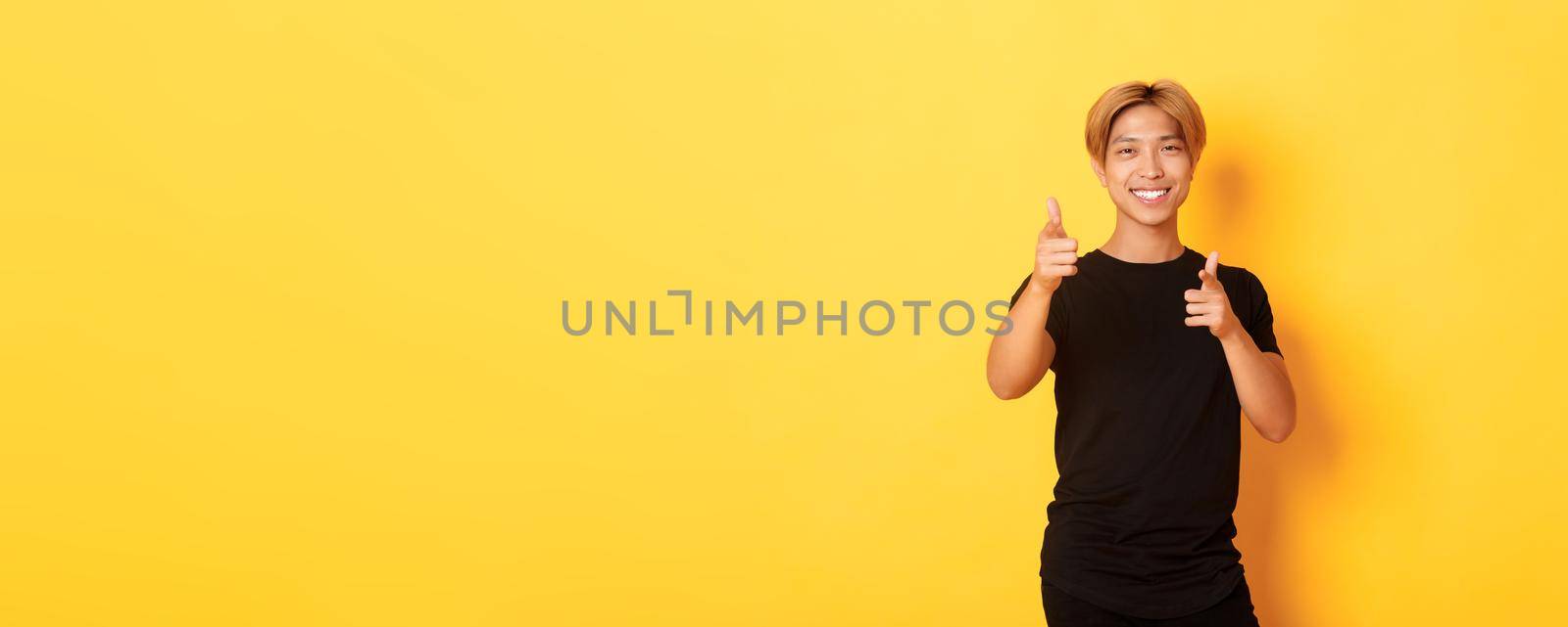 Portrait of cheeky smiling asian guy, looking satisfied and pointing fingers at camera, praising something or making compliment.