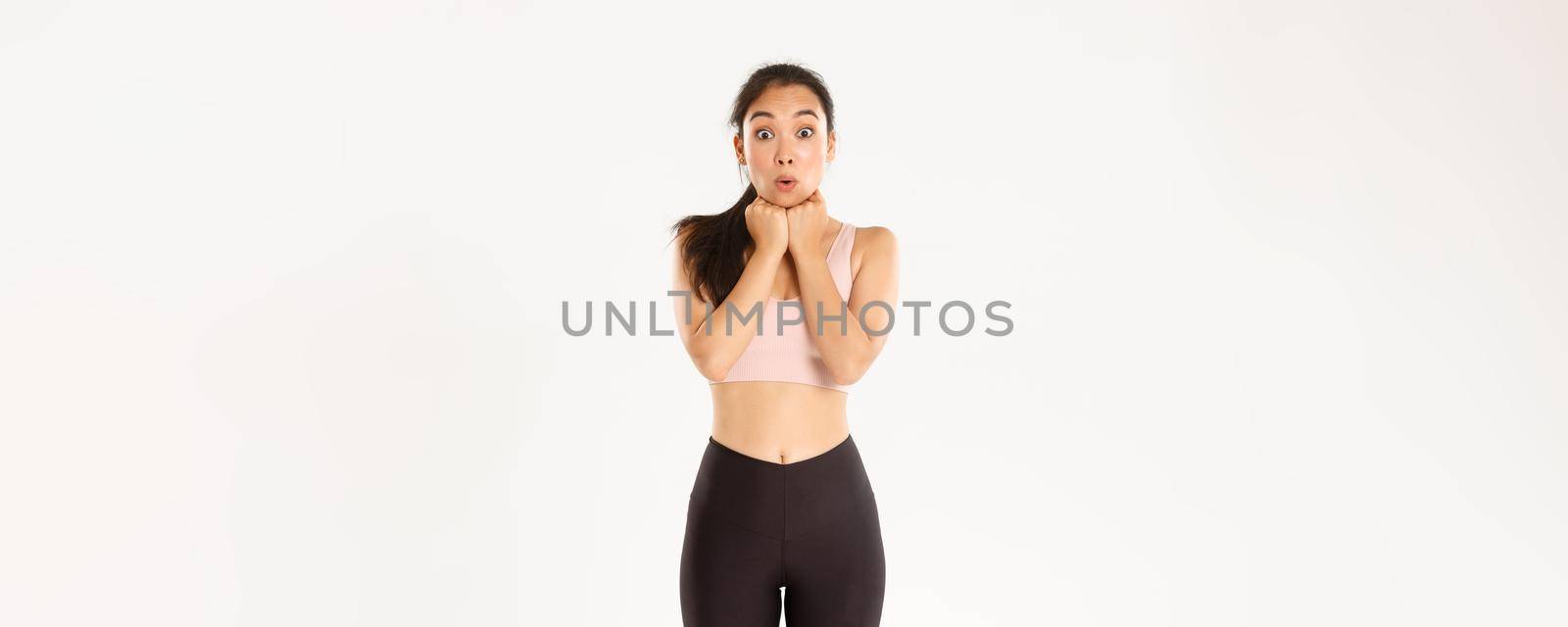 Sport, wellbeing and active lifestyle concept. Excited and amazed, thrilled asian fitness girl in activewear looking at discount banner, special offer advertisement, standing white background by Benzoix