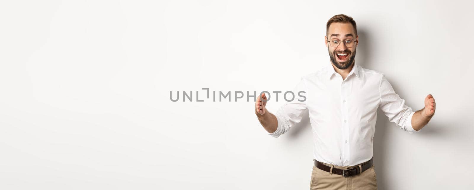 Amazed businessman showing big object, describe something large and looking excited, standing over white background.