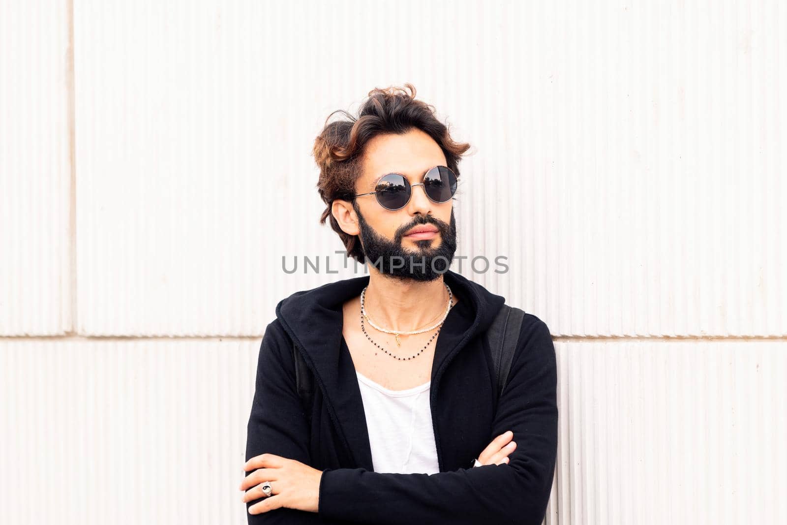 beautiful young man with sunglasses leaning in a white wall, concept of urban lifestyle and stylish clothing, copy space for text