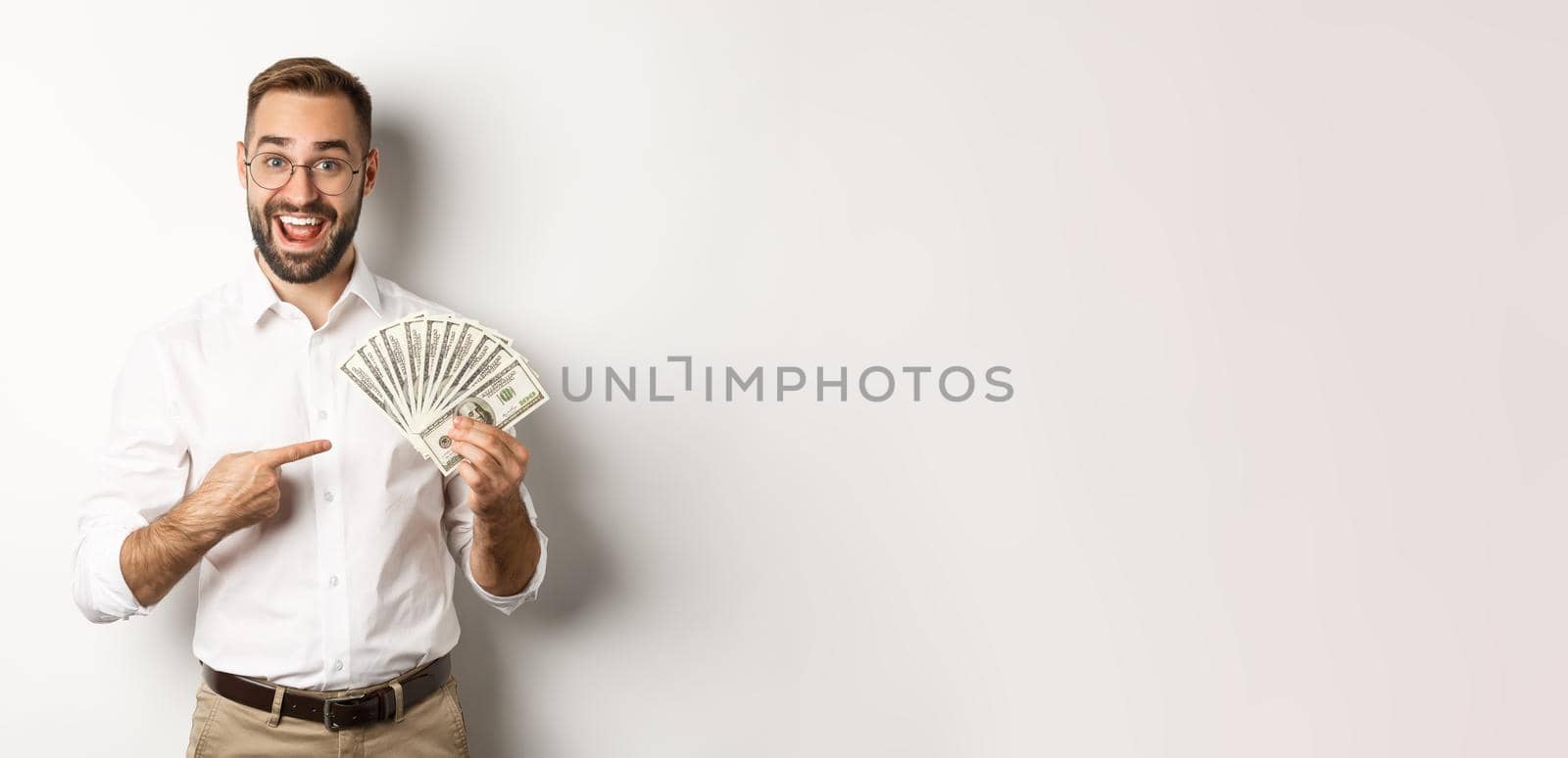 Excited businessman pointing at money, showing dollars and smiling, standing over white background by Benzoix