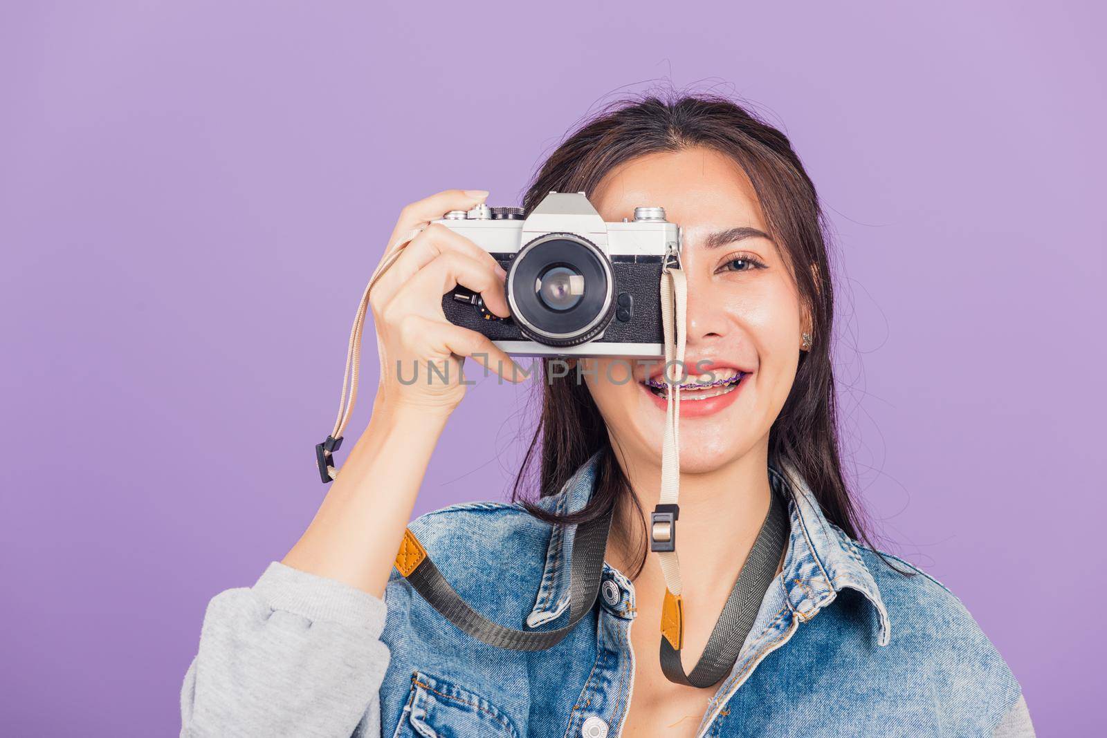 Portrait happy beautiful young woman smile excited wear denims photographer taking a picture and looking viewfinder on vintage photo camera ready to shoot, studio shot isolated on purple background