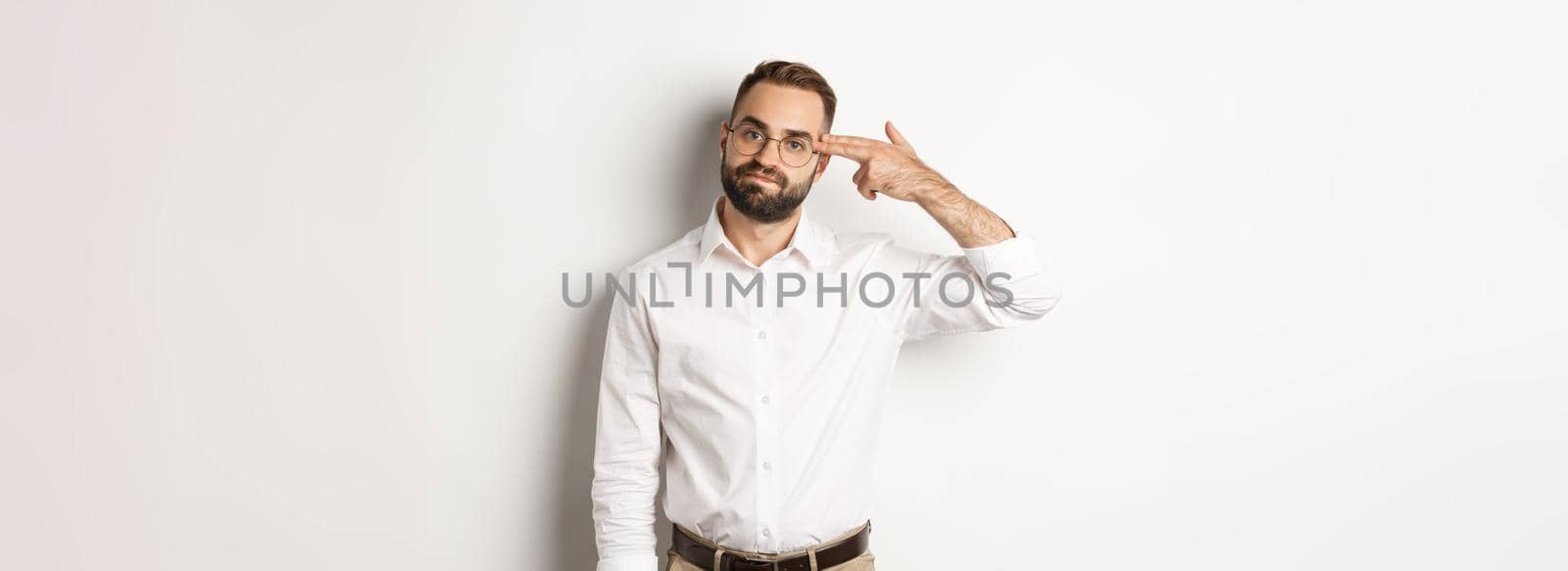 Tired man making shooting in head and looking bored, standing distressed over white background.