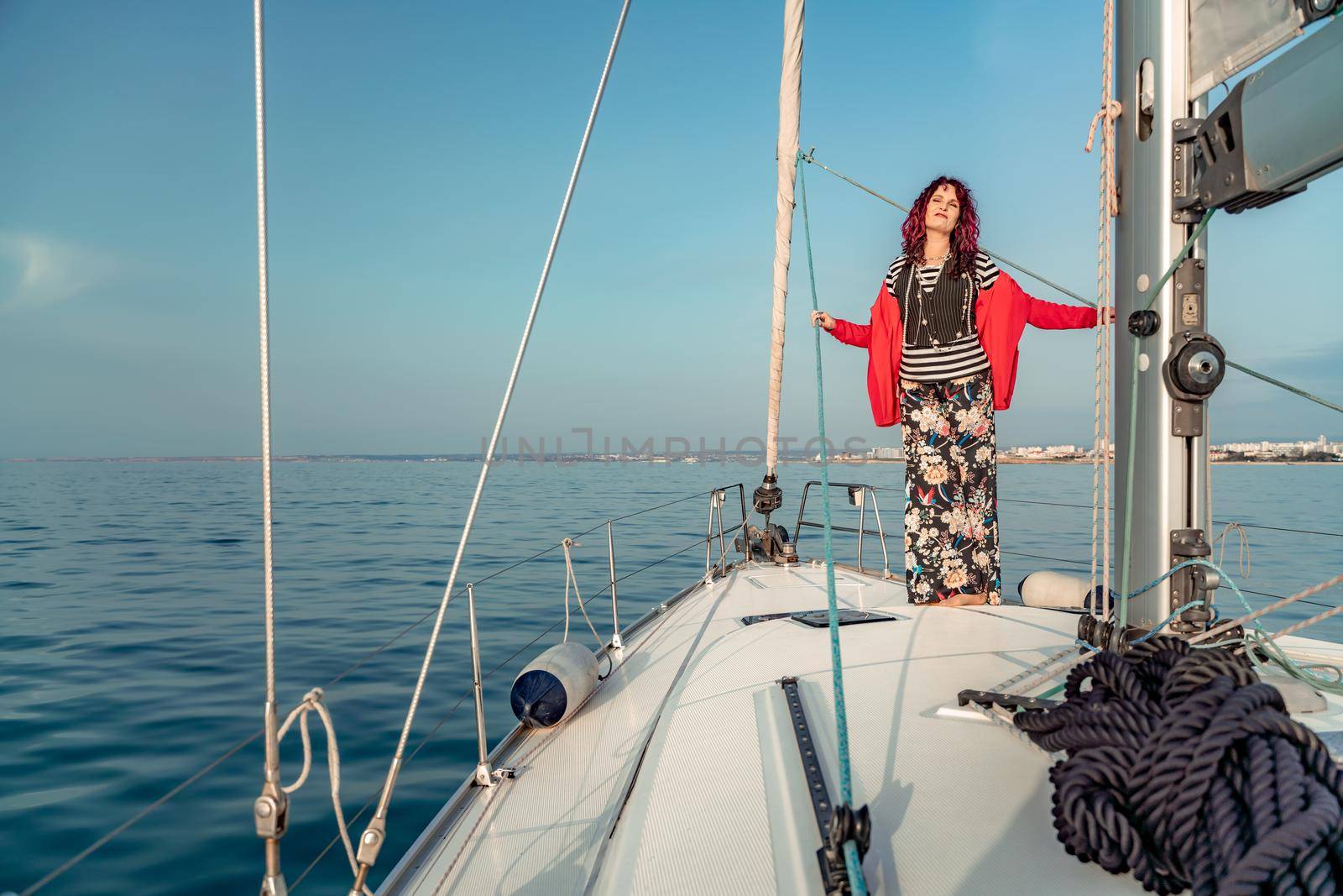 Woman standing on the nose of the yacht at a sunny summer day, breeze developing hair, beautiful sea on background by Matiunina