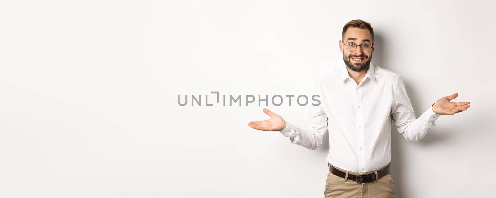 Confused smiling businessman dont know, shrugging and saying sorry, standing over white background by Benzoix